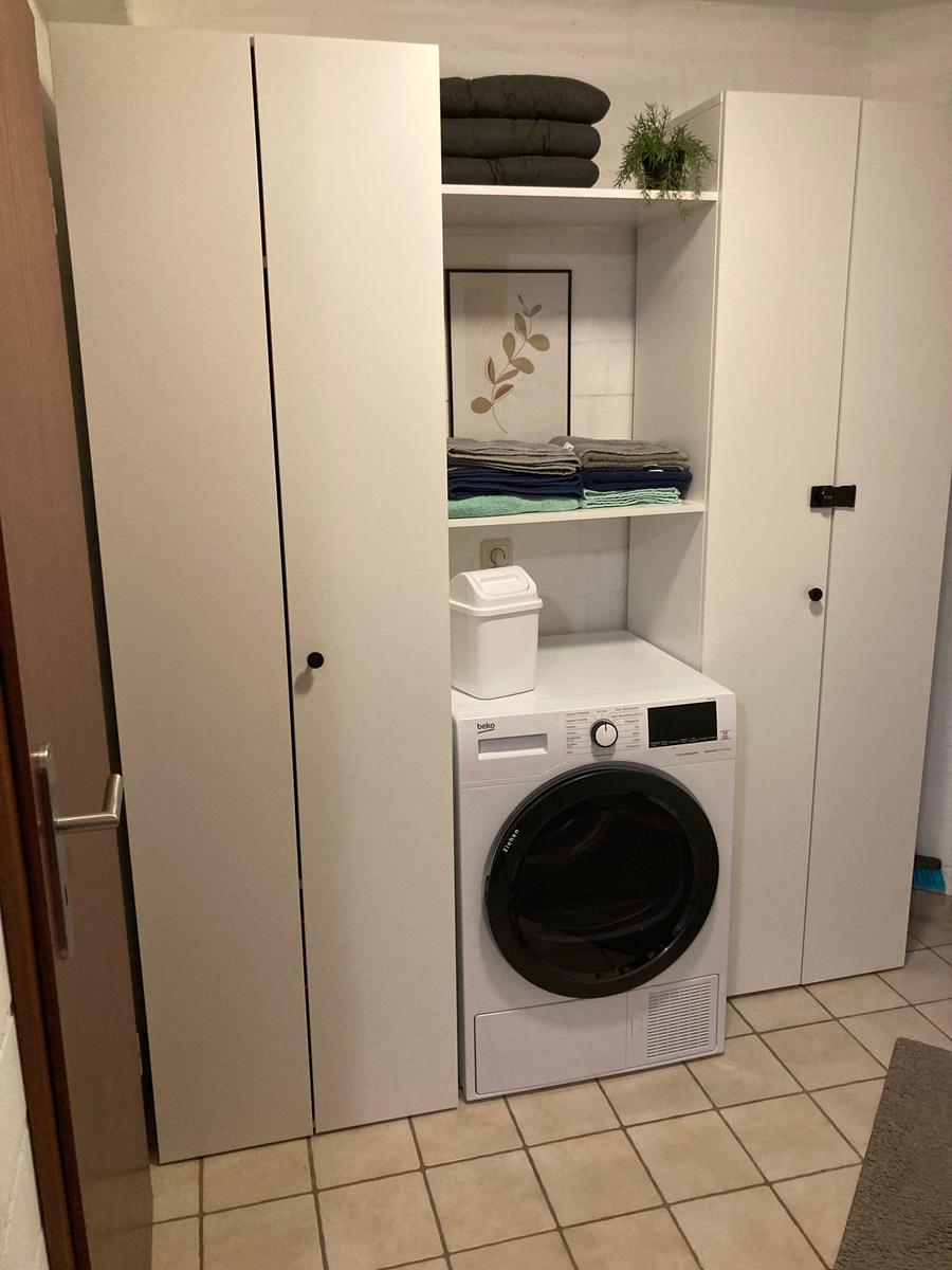 Waschmaschine in einem Raum mit weißen Schränken und gefalteten Handtüchern.