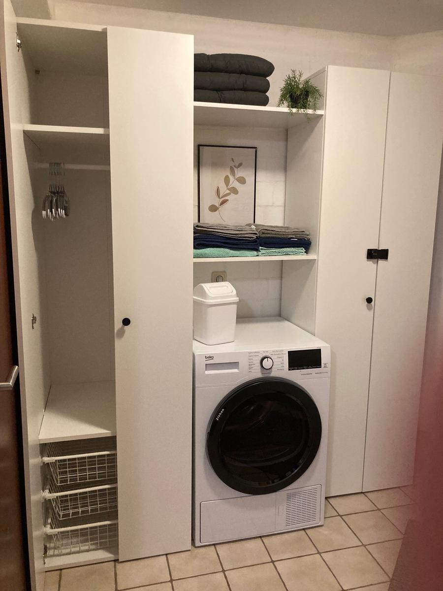 Wäschetrockner in weißem Schrank mit Regalen und Handtüchern.