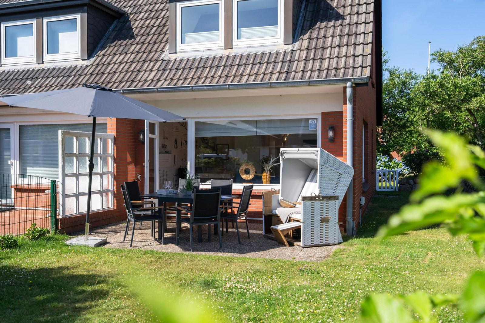Haus mit Terrasse, Tisch, Stühlen und Strandkorb im Garten.
