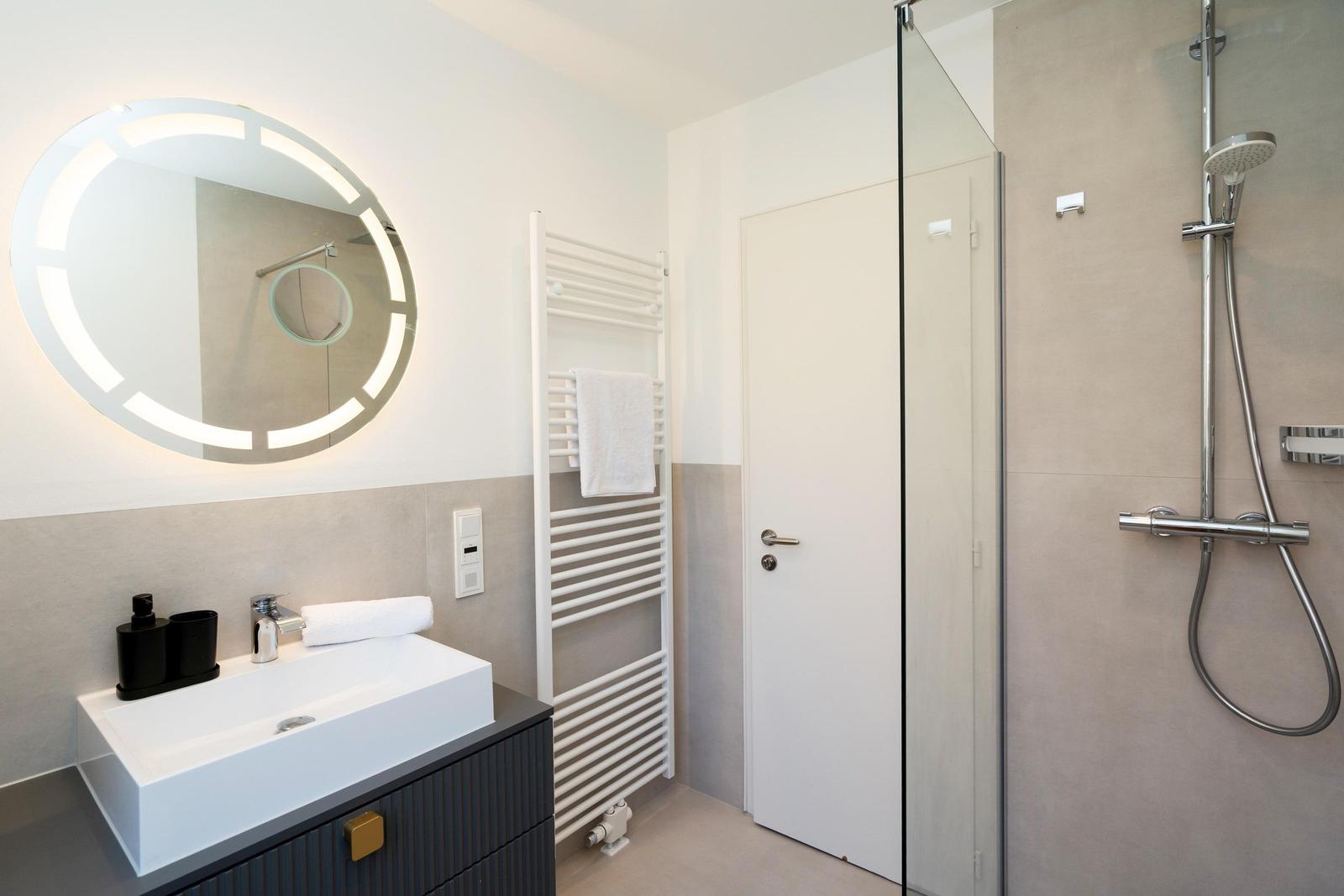 Badezimmer mit Dusche, Waschbecken und Heizkörper.