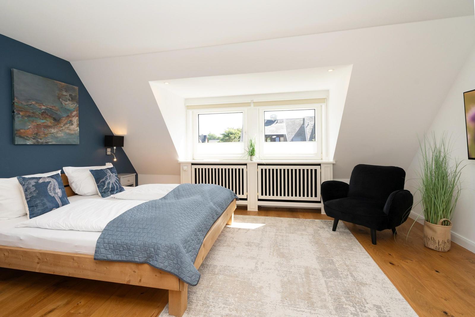 Schlafzimmer mit Dachschrägen, Bett, Sessel und Fenster.