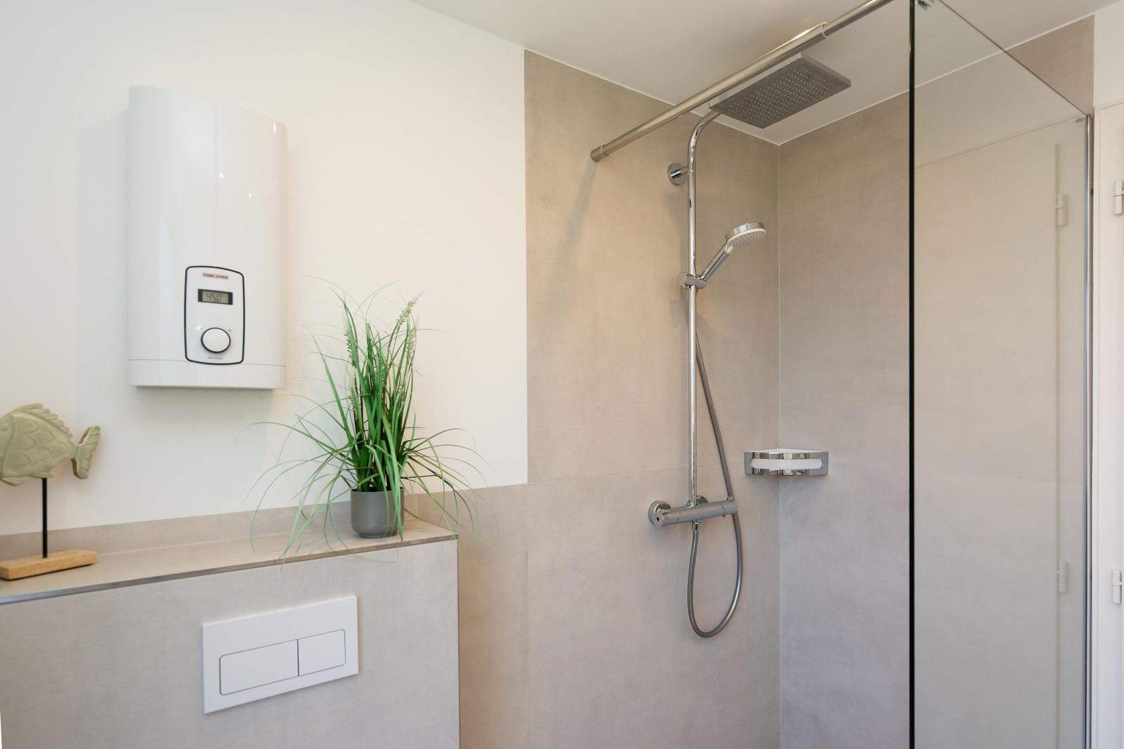 Dusche mit Glaswand, Duschbrause und Heizung an der Wand.
