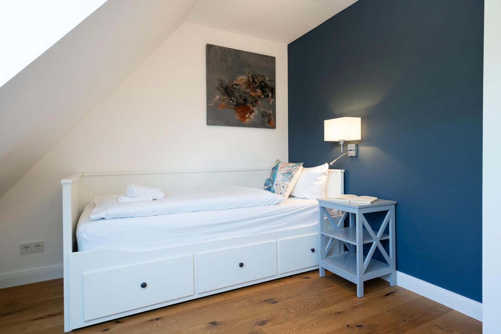 Schlafzimmer mit weißem Bett, blauer Wand und Nachttisch