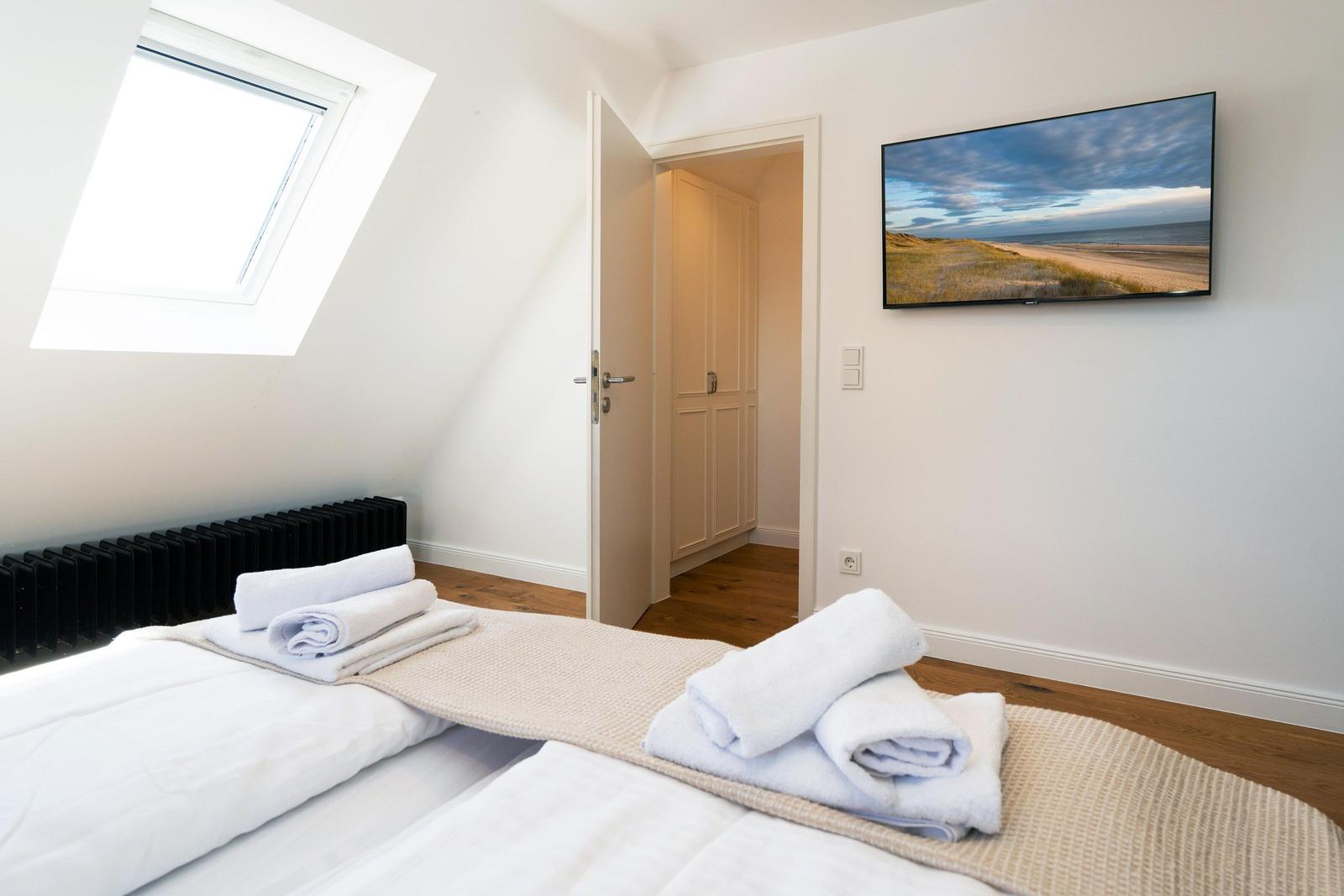 Schlafzimmer mit Dachschräge, Dachfenster, Bett und Fernseher an der Wand.