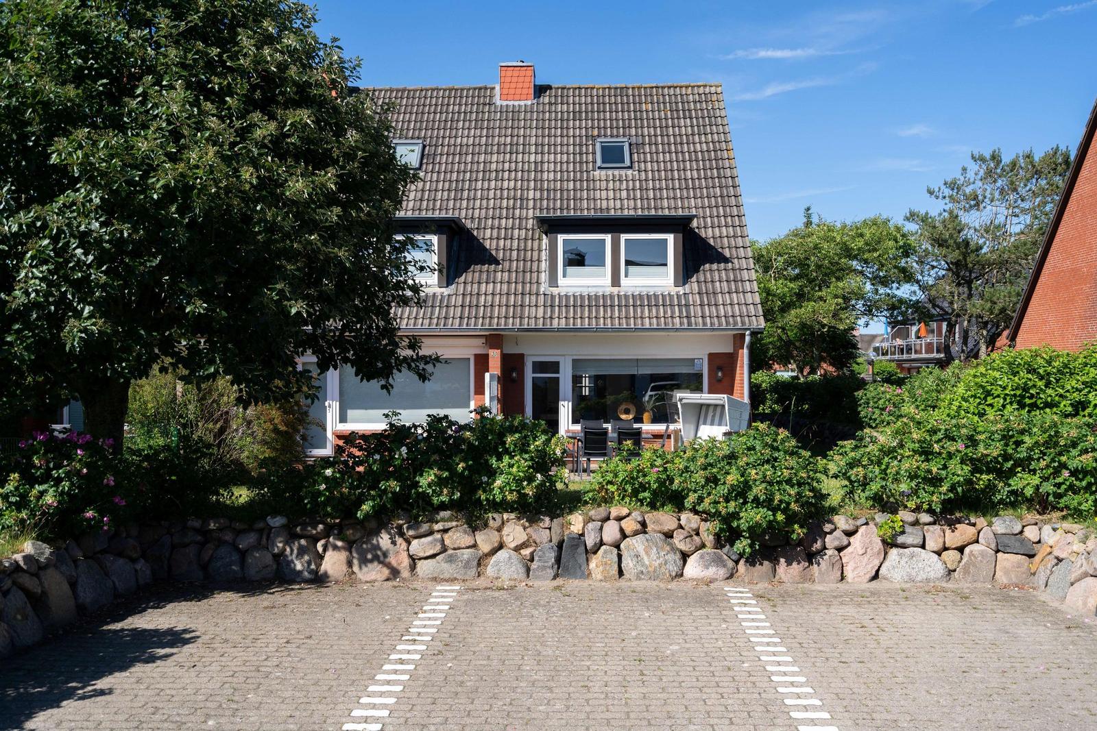 Haus mit Steinmauer, gepflasterter Hof und grüner Umgebung unter blauem Himmel.