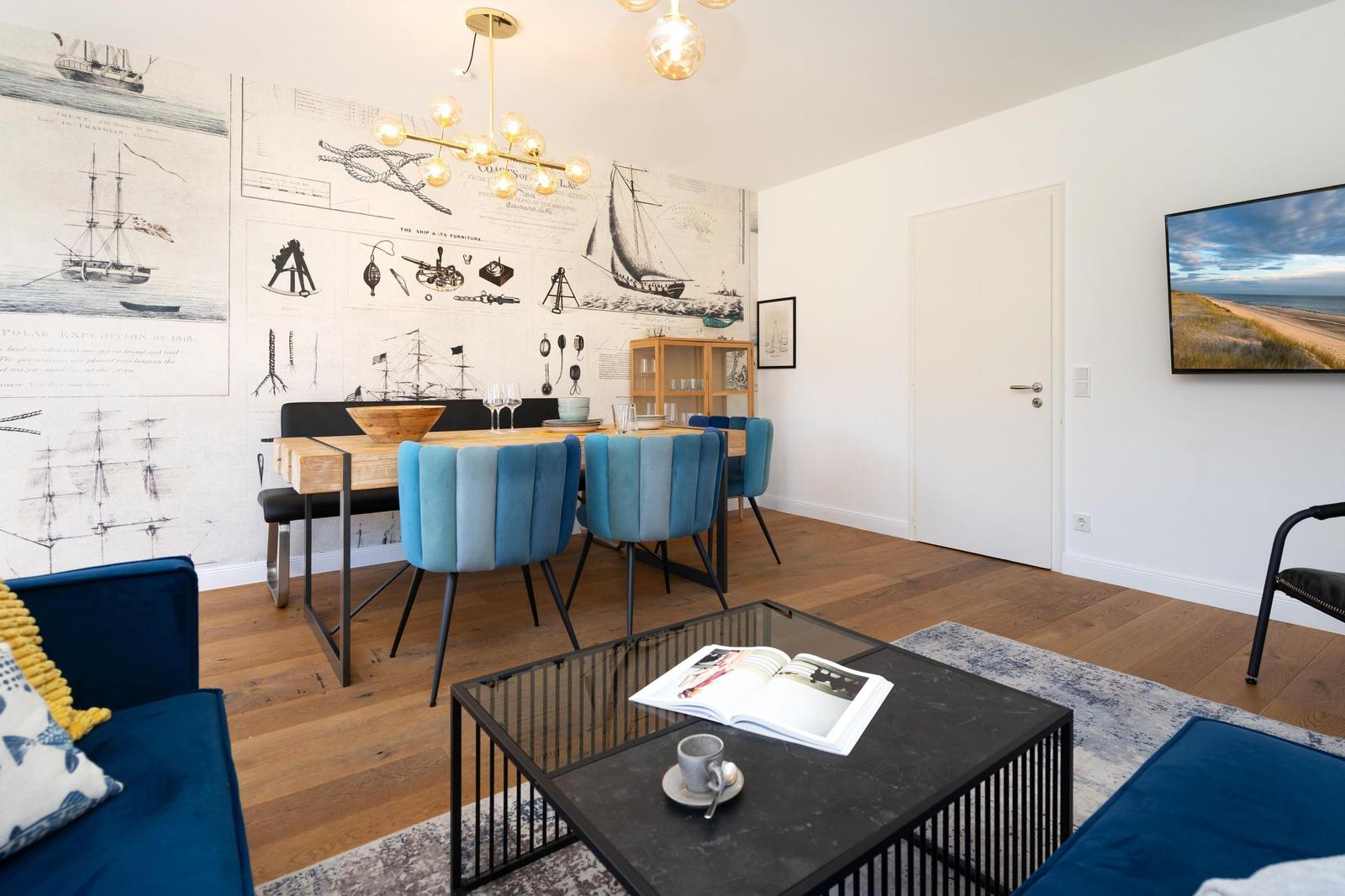 Essbereich mit blauen Stühlen und Schiffsmotiven an der Wand. Wohnbereich mit Couch und Couchtisch.