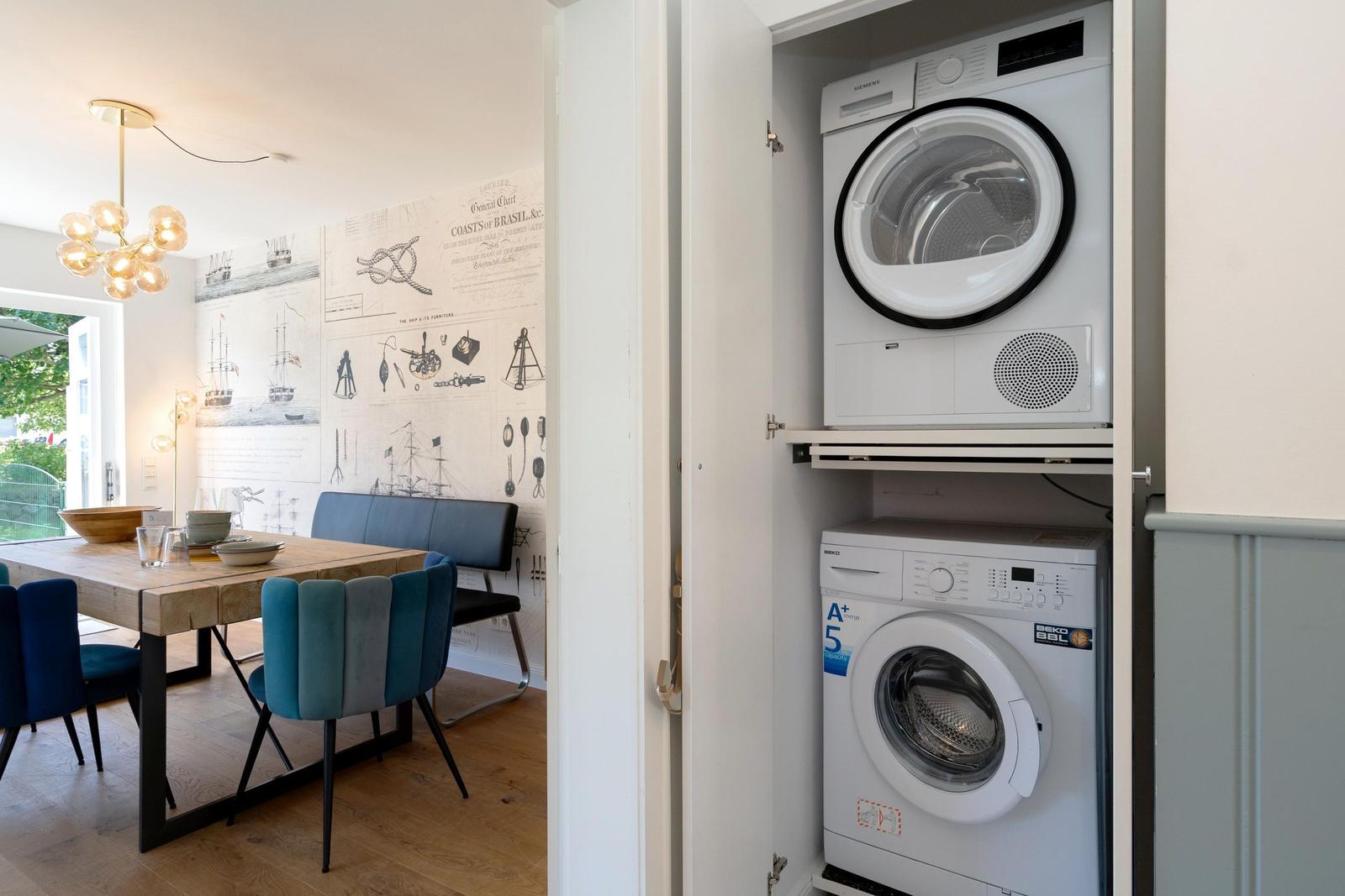 Wäschetrockner und Waschmaschine in einem Schrank. Im Hintergrund ein Essbereich mit Tisch und Stühlen.