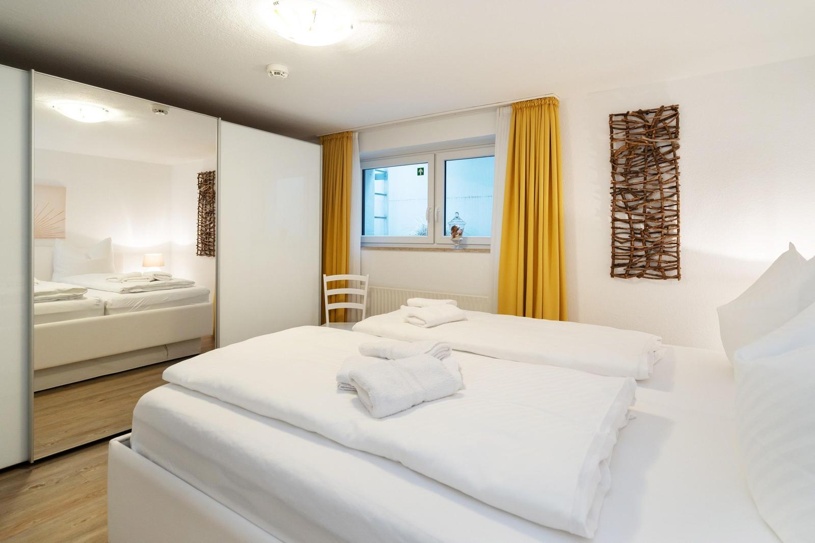 Zimmer mit zwei Betten, gelben Vorhängen und Spiegelschrank.