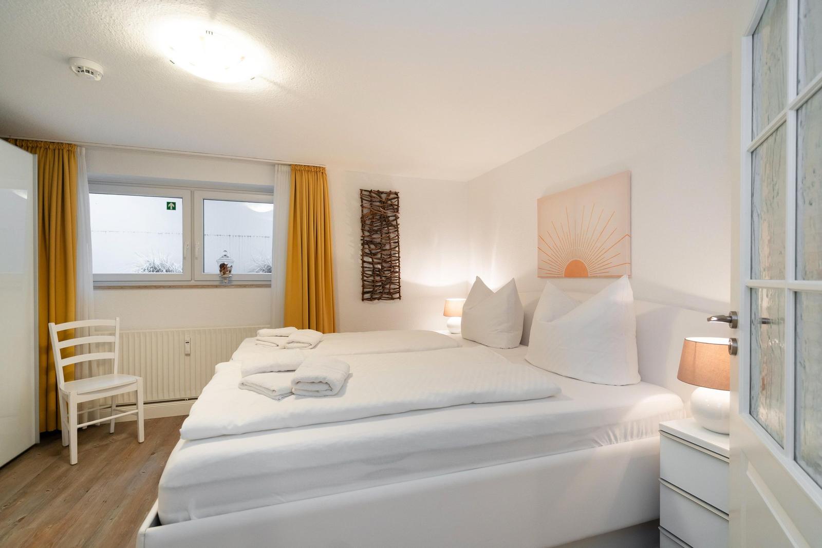 Schlafzimmer mit weißem Bett, gelben Vorhängen und Wandkunst.
