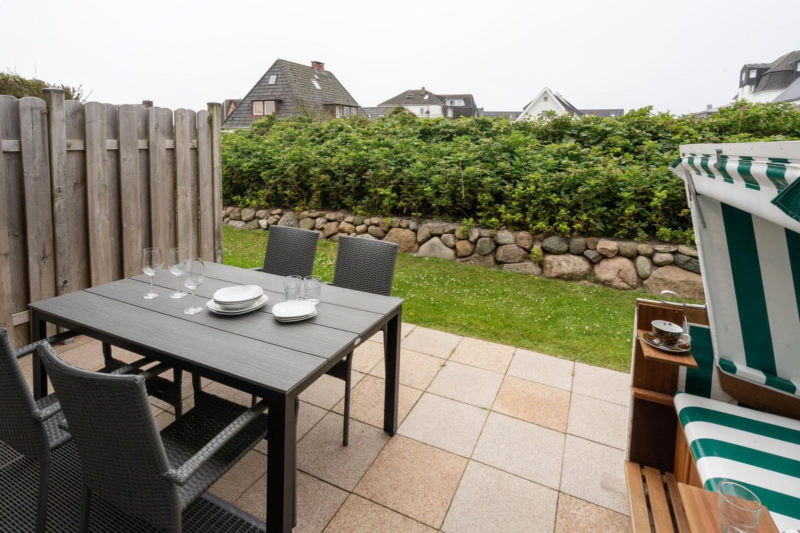 Terrasse mit Tisch, Stühlen und Liege. Hinterhof mit Rasen und Hecke.