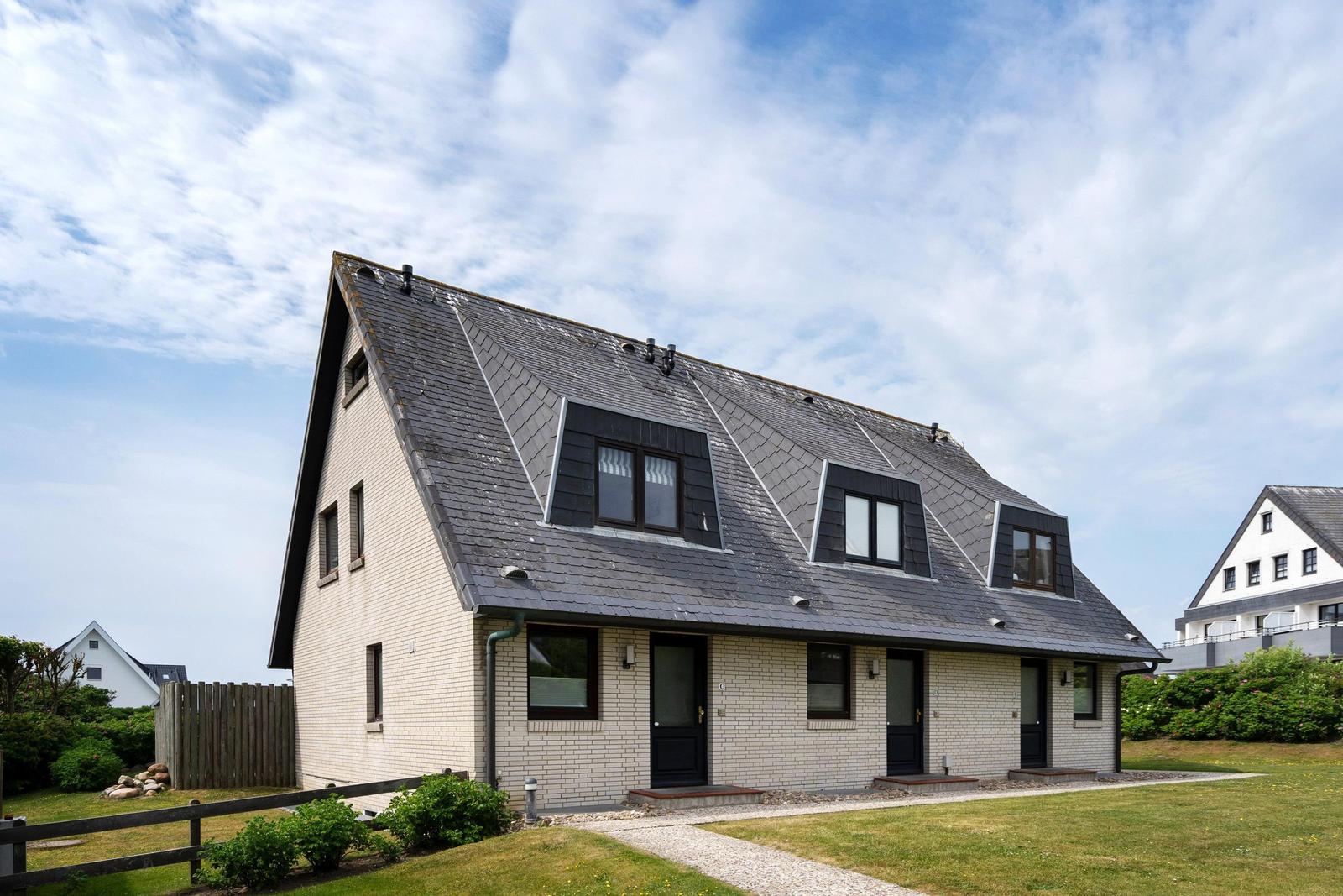 Ein modernes Haus mit grauem Dach und hellen Wänden. Mehrere Fenster und Türen sind sichtbar.