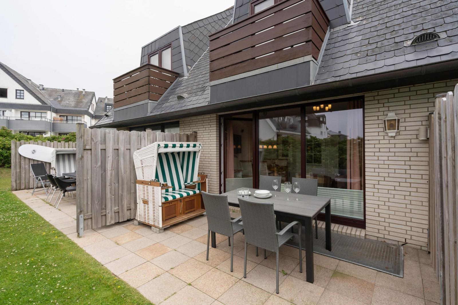Terrasse mit Esstisch, Liegestuhl und Garten. Modernes Haus mit Holz- und Ziegelaufbau.
