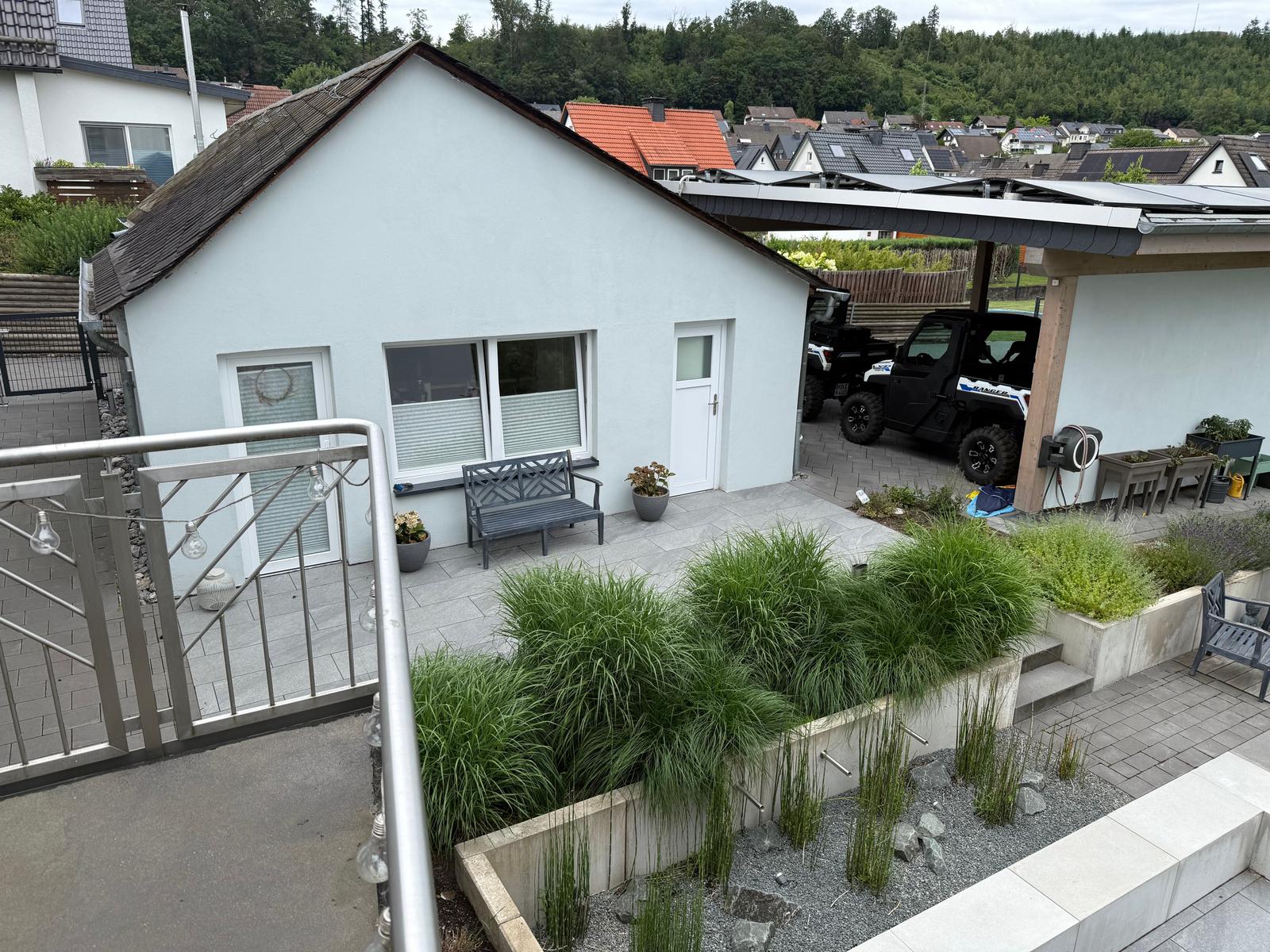 Haus mit Terrasse, Garten und geparktem Geländewagen. Blick auf Wohngebiet und Wald.