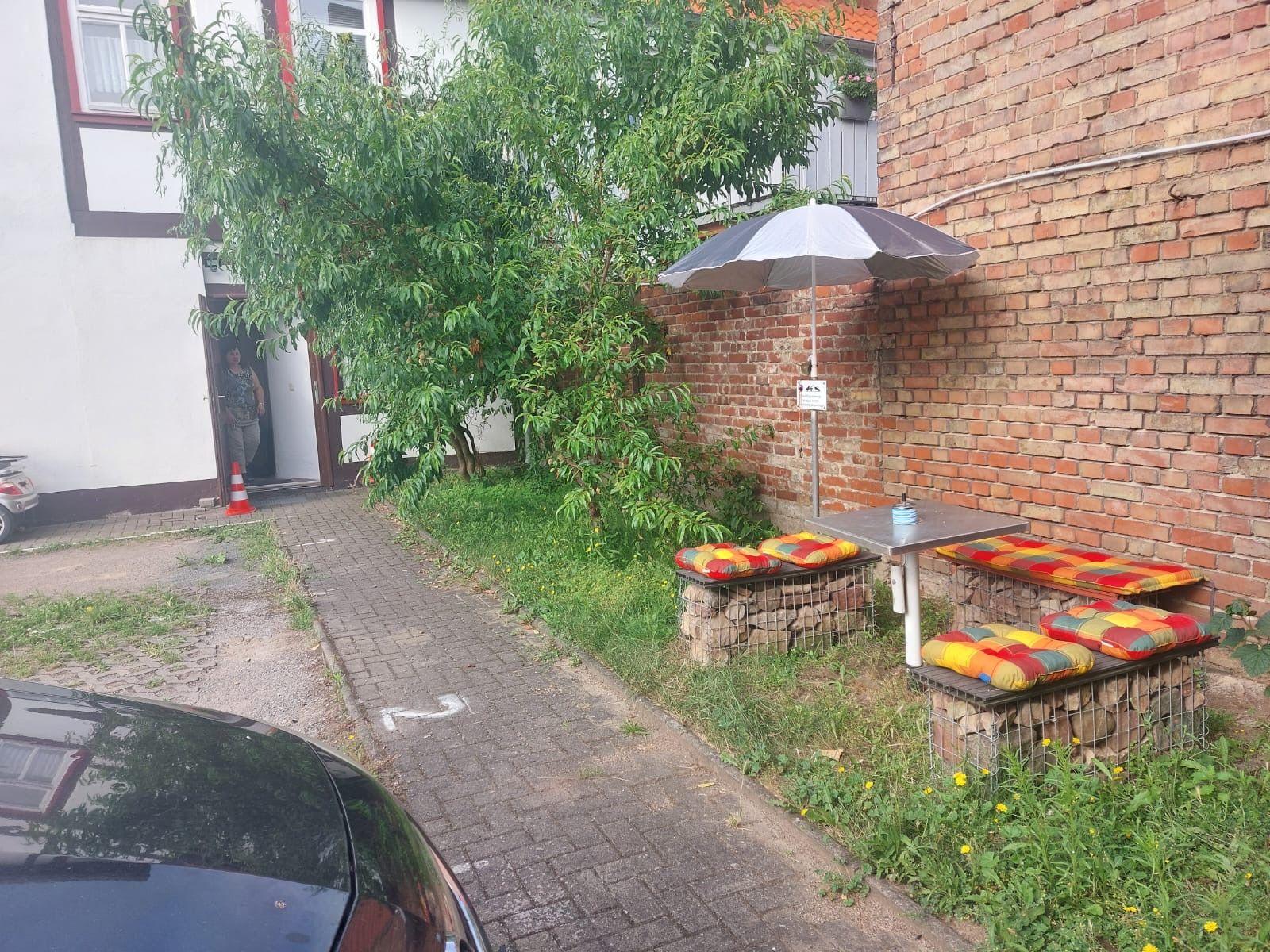 Außenbereich mit Tisch, Sitzbänken und Sonnenschirm an Backsteinmauer.