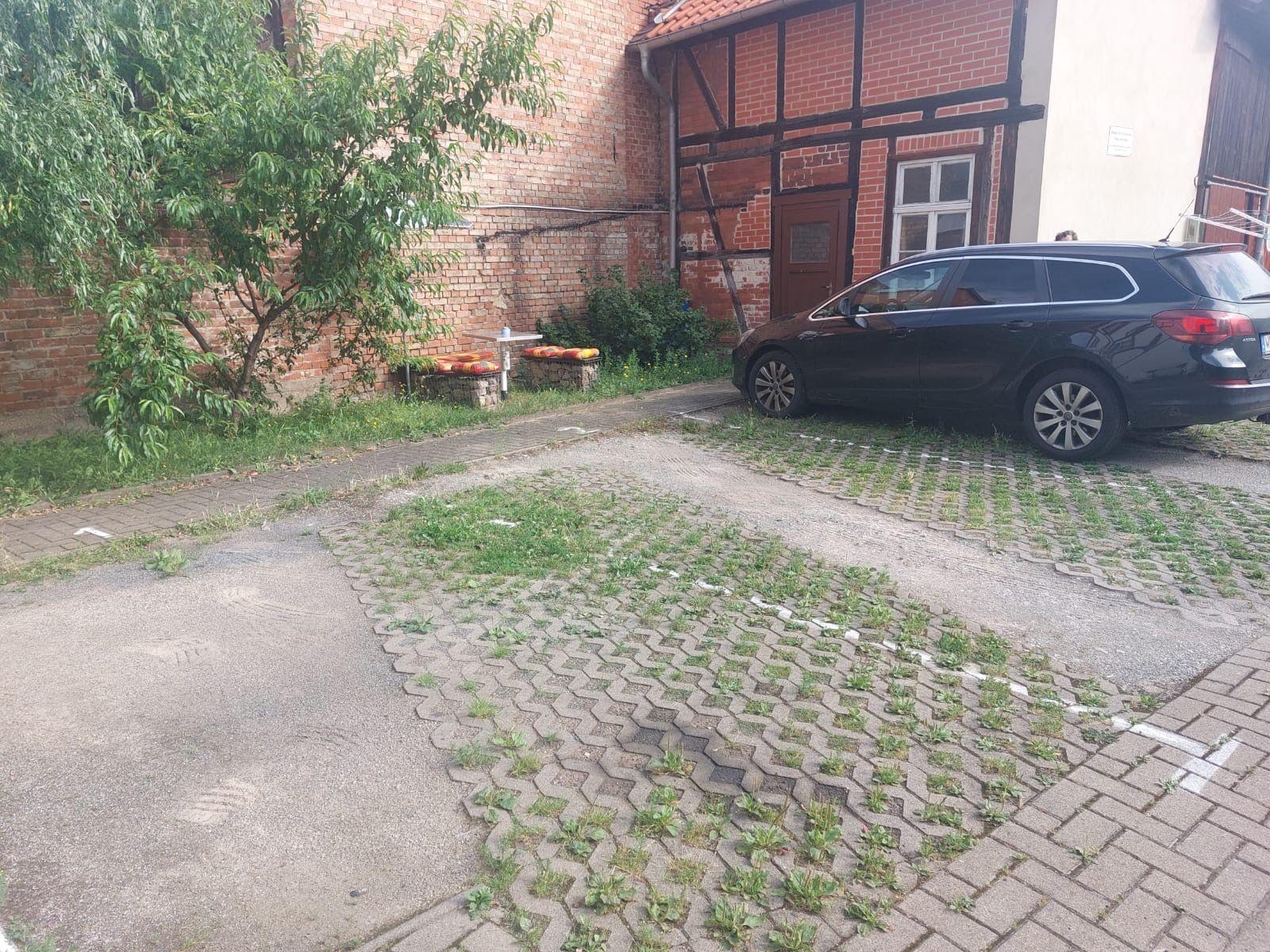 Vorhof mit gepflastertem Bereich, einem Baum und einem parkenden Auto.