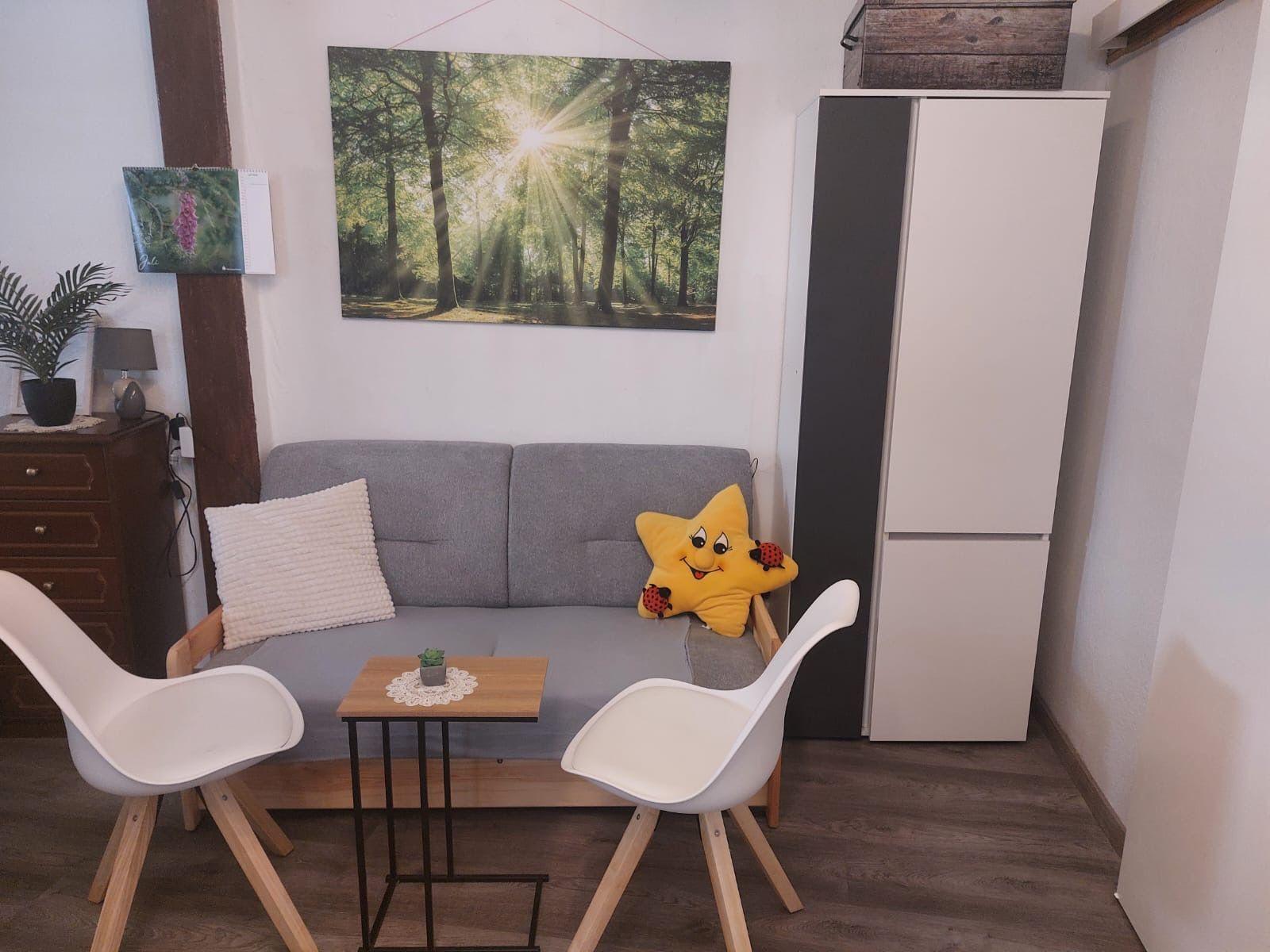 Graße Couch mit Kissen, zwei weiße Stühle und kleiner Tisch.