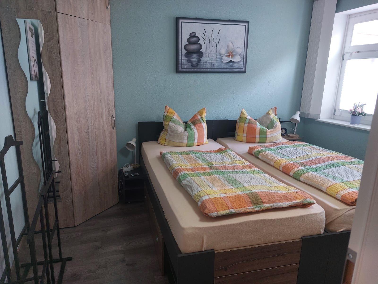 Zwei Einzelbetten mit bunten Decken und Kissen. Wandbild, Fenster und Kleiderschrank.