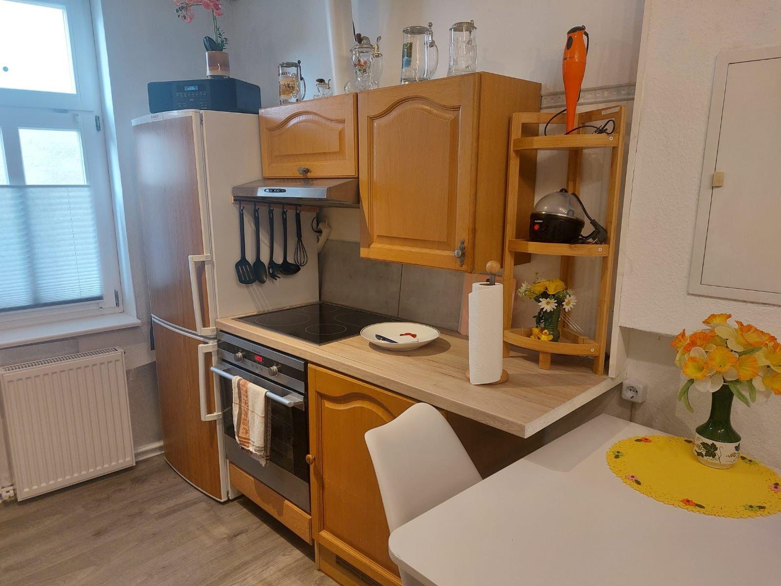 Küche mit Holzschränken, Kühlschrank, Herd und Esstisch mit Blumen.