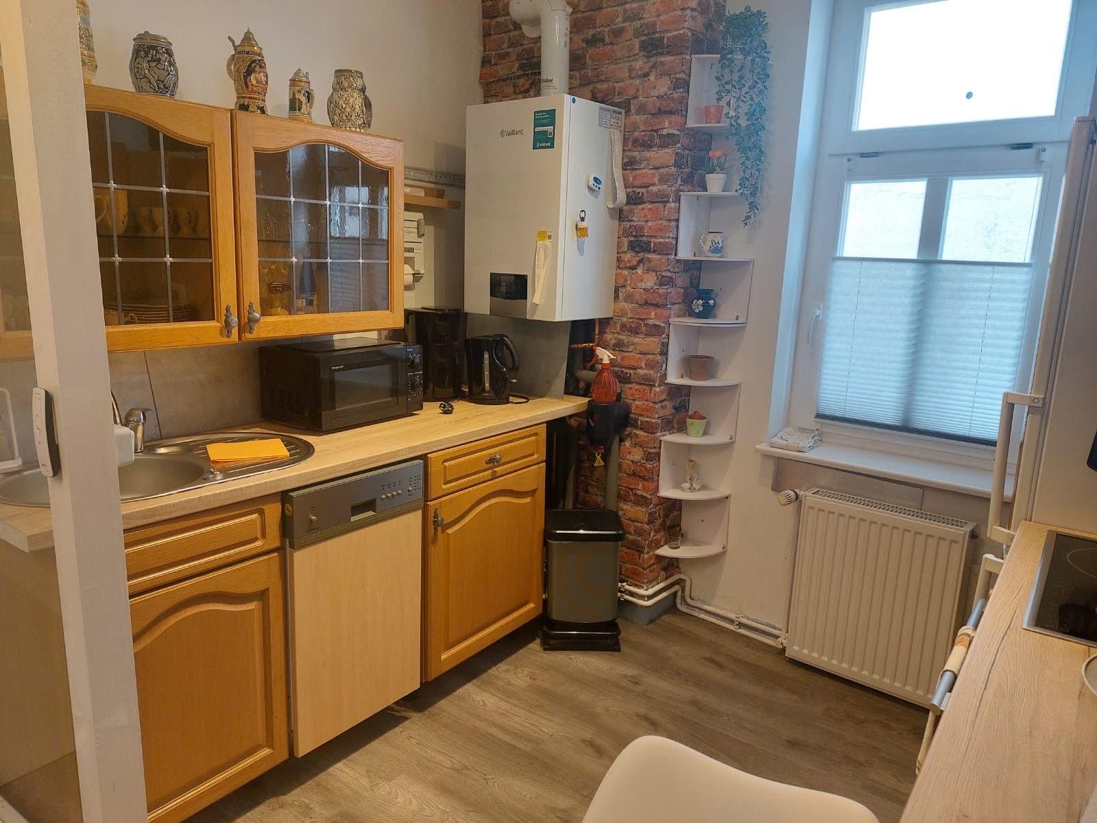 Küche mit Holzschränken, Spüle, Mikrowelle und Kühlschrank an der Backsteinwand.