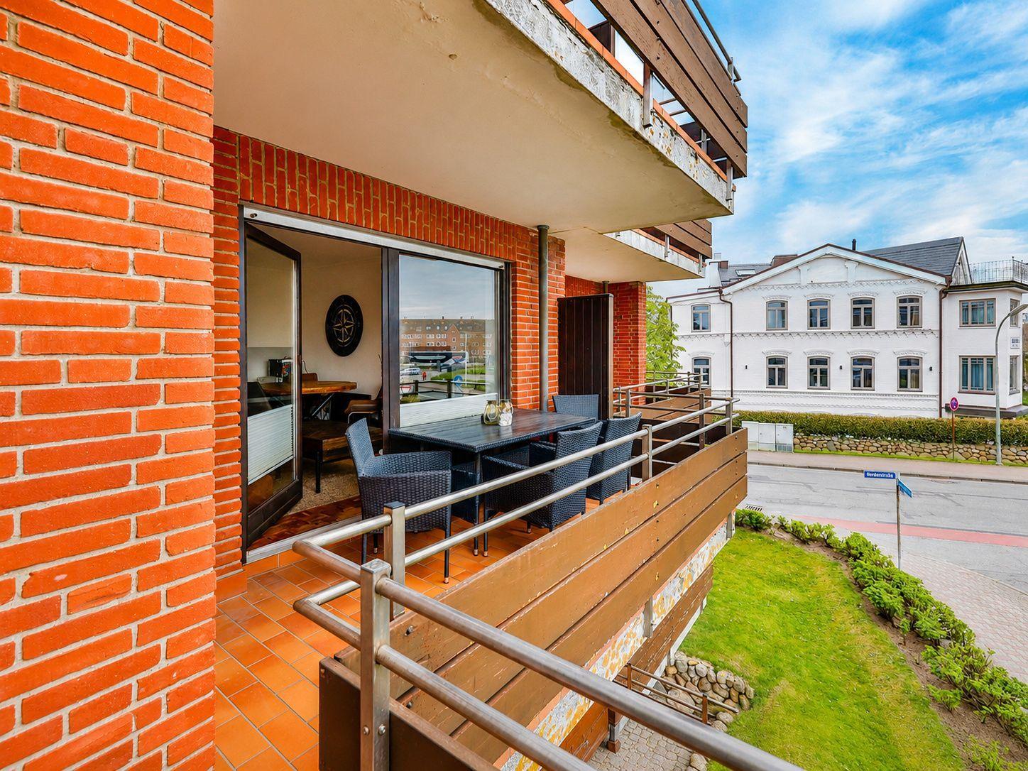 Terrasse mit Tisch und Stühlen, Blick auf Straße und weißes Gebäude.
