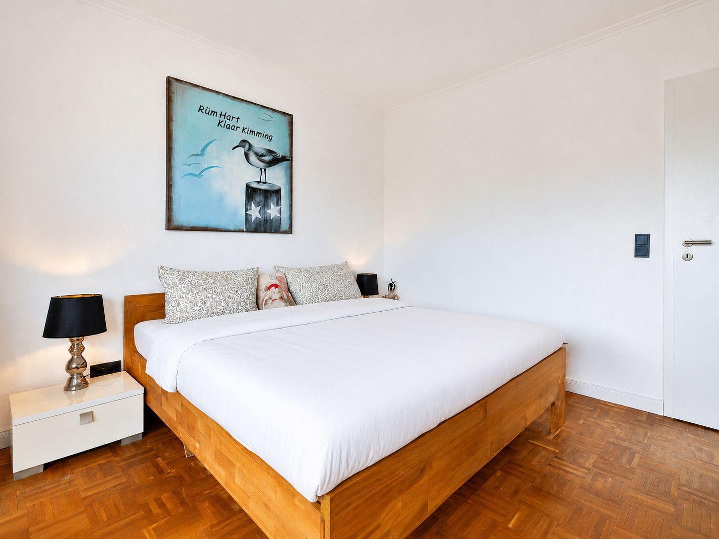 Schlafzimmer mit Holzbett, weißen Kissen und Wandbild mit Möwe.