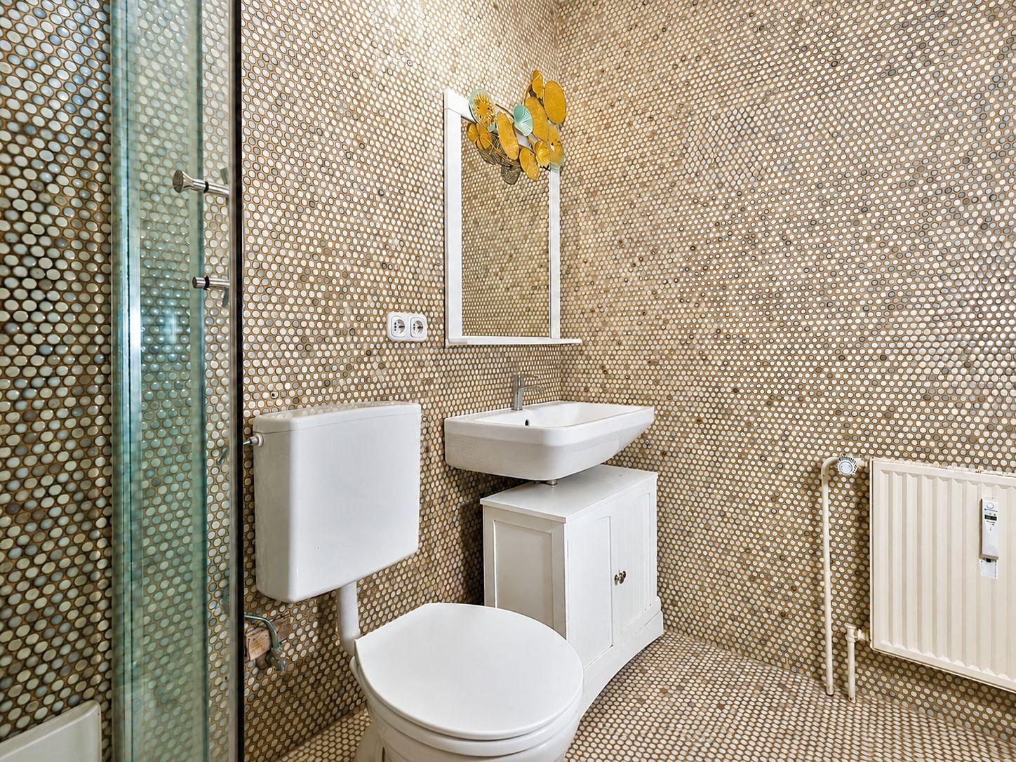 Badezimmer mit Toilette, Waschbecken und Dusche. Wände und Boden mit Mosaik verkleidet.