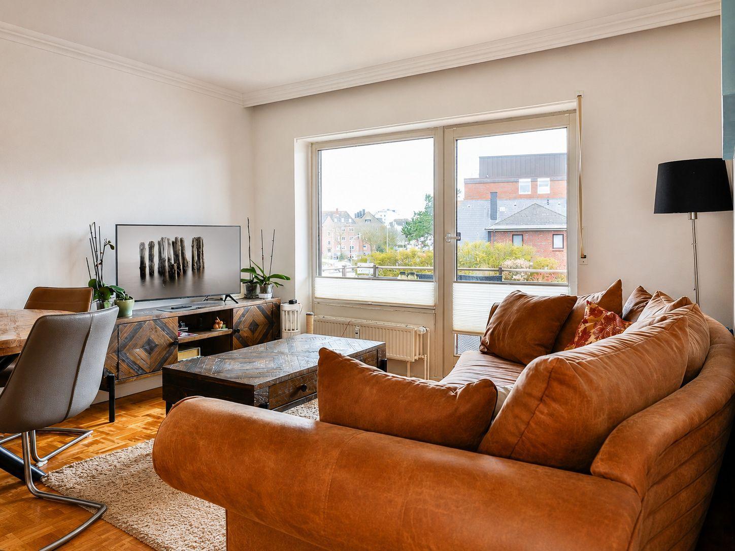 Wohnzimmer mit braunem Sofa, Fernseher und Blick auf Balkon.