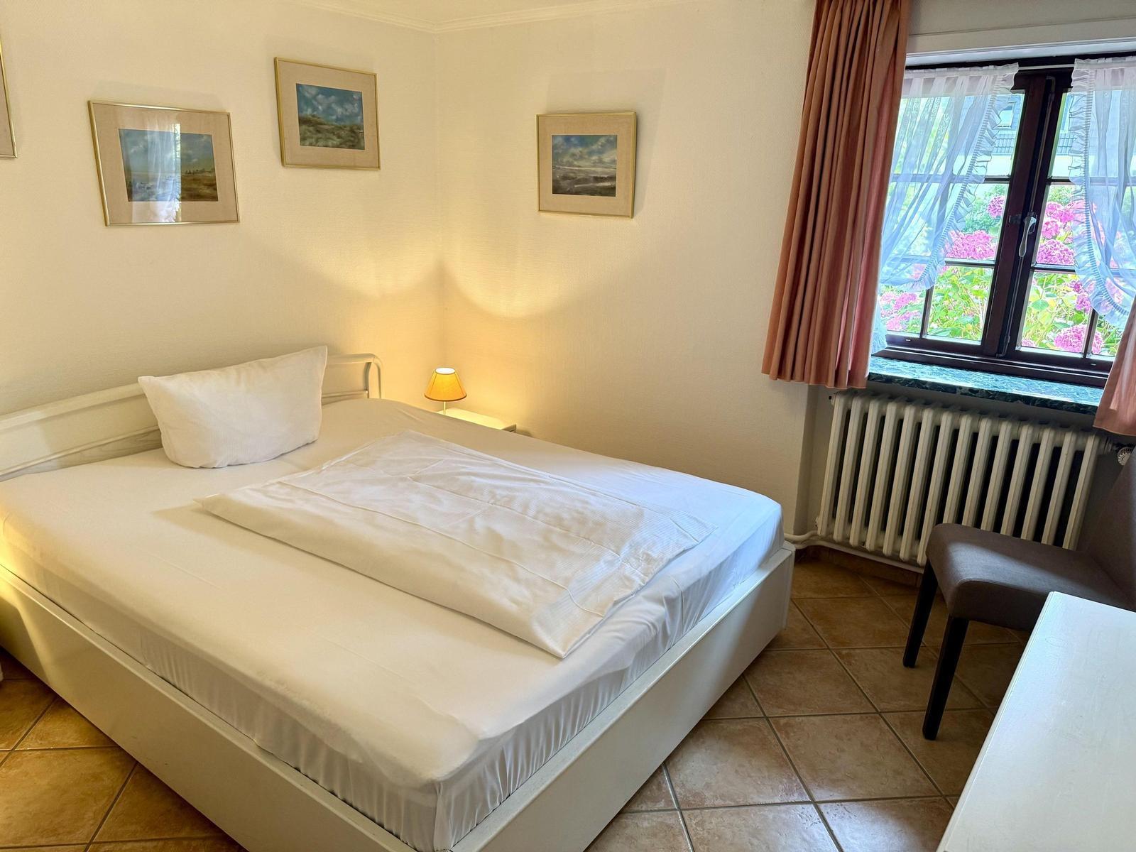 Bedroom with bed, window, and pictures on the wall.