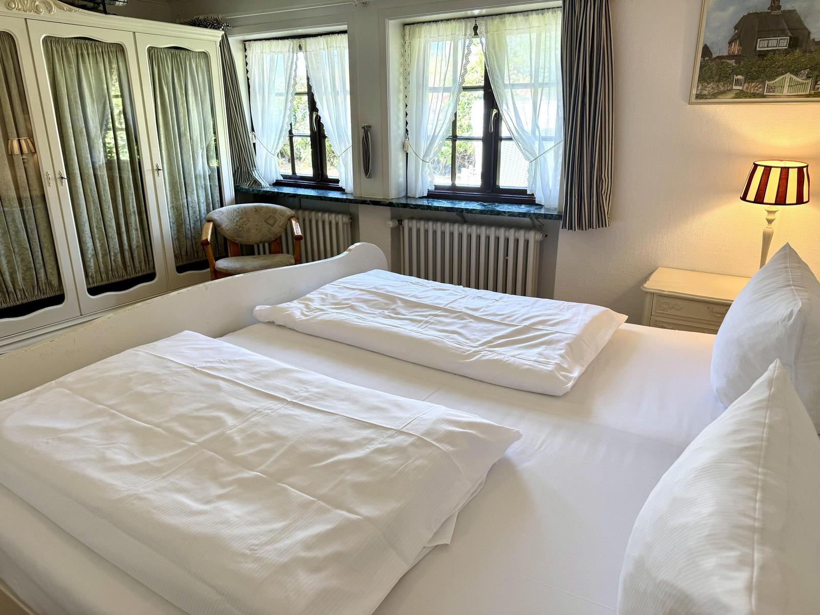 Bedroom with double bed, windows, wardrobe, and nightstand.