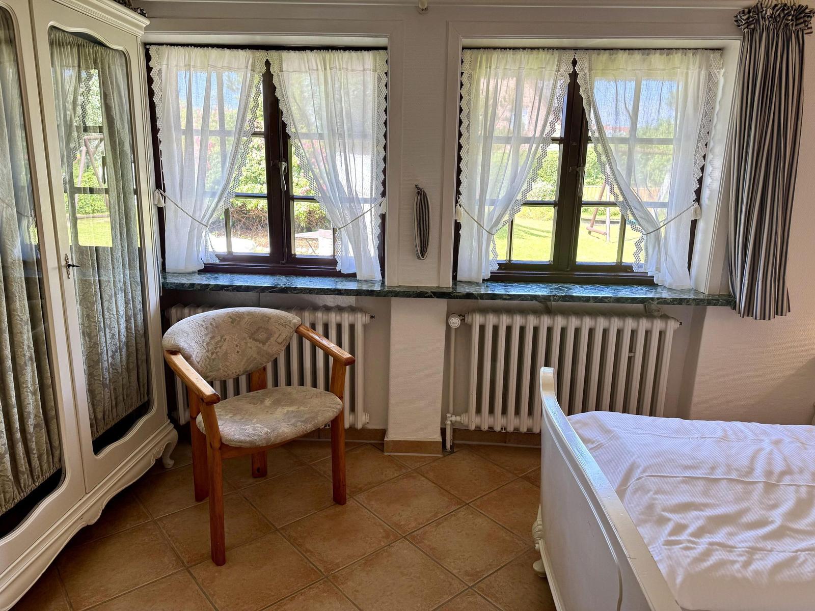 Bedroom with bed, chair, and two windows with curtains.