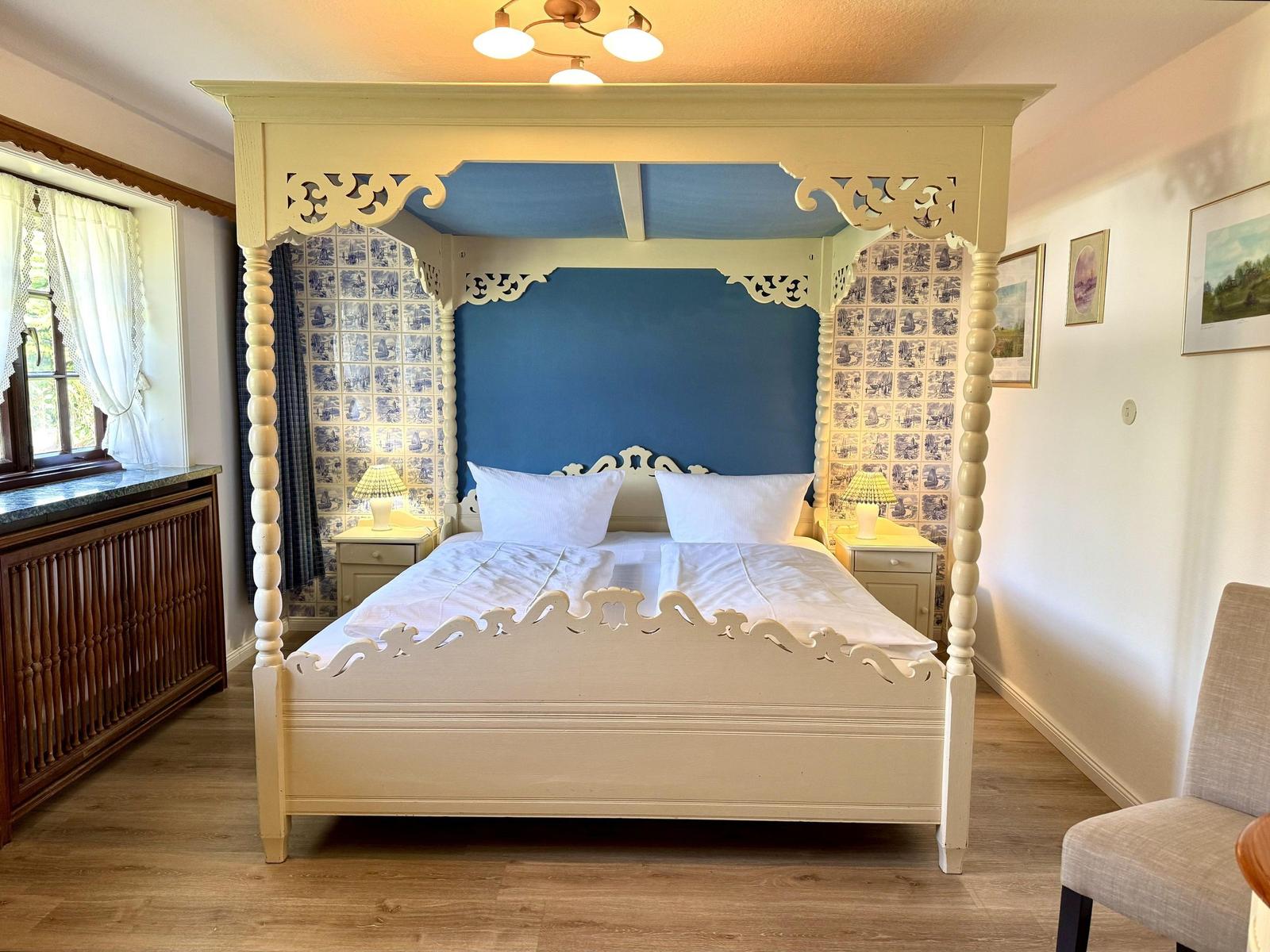 Bedroom with four-poster bed, blue wall, and wooden floor.