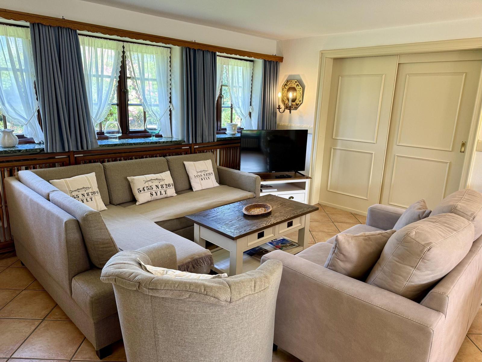 Living room with sofa, couch, and TV. Windows with curtains and wooden table.