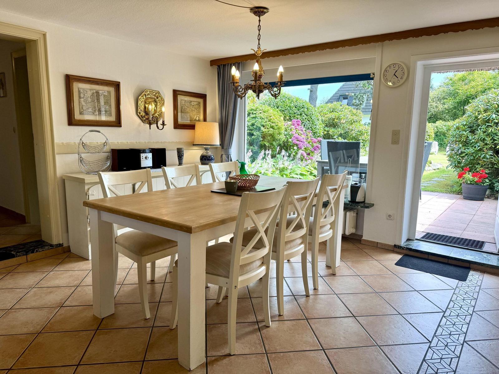 Dining room with wooden table, white chairs, and view of garden