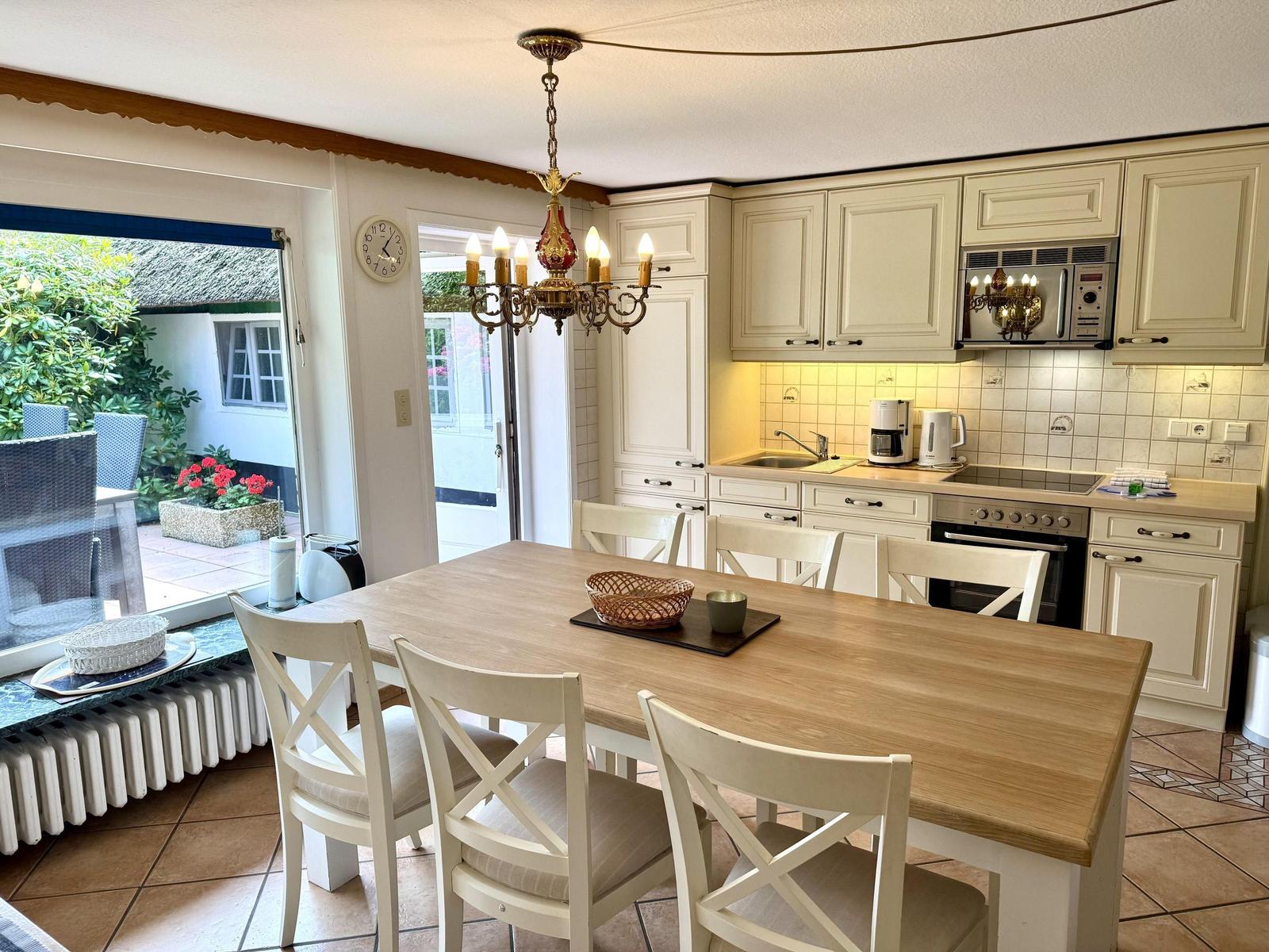 Kitchen with dining table, white chairs, and view to balcony.
