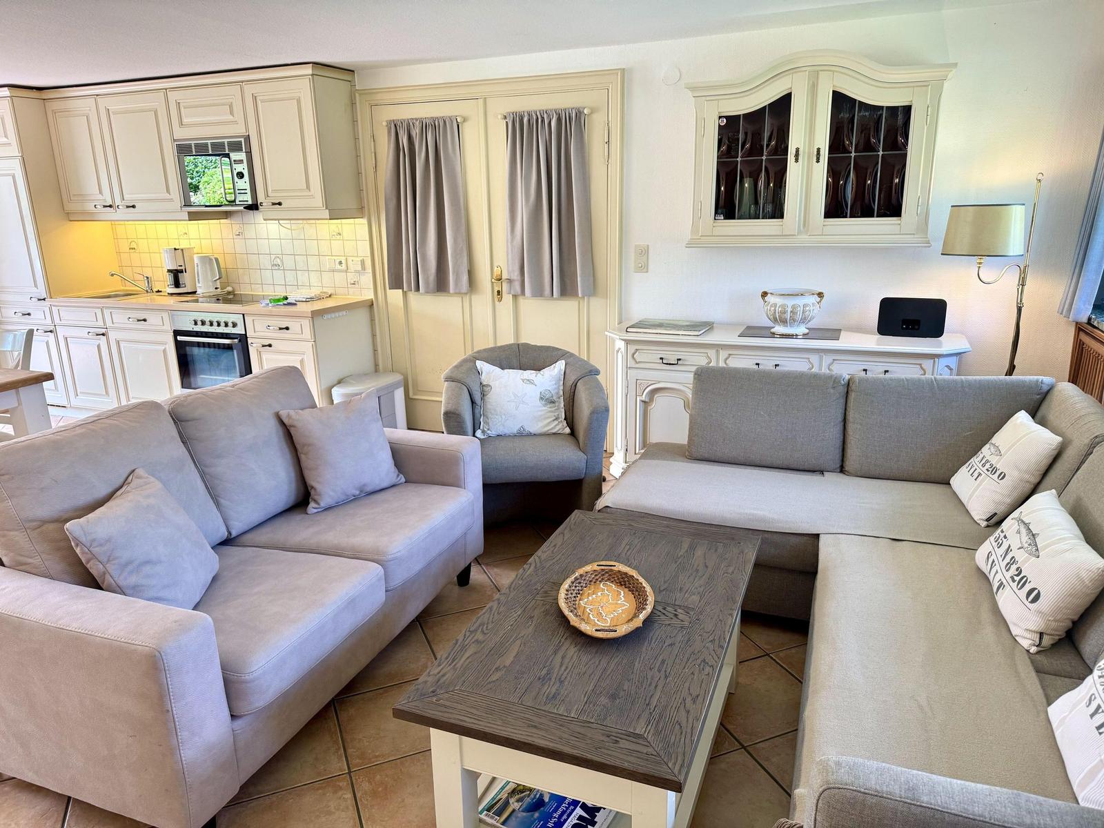 Living and kitchen area with sofa, armchair, and kitchenette.