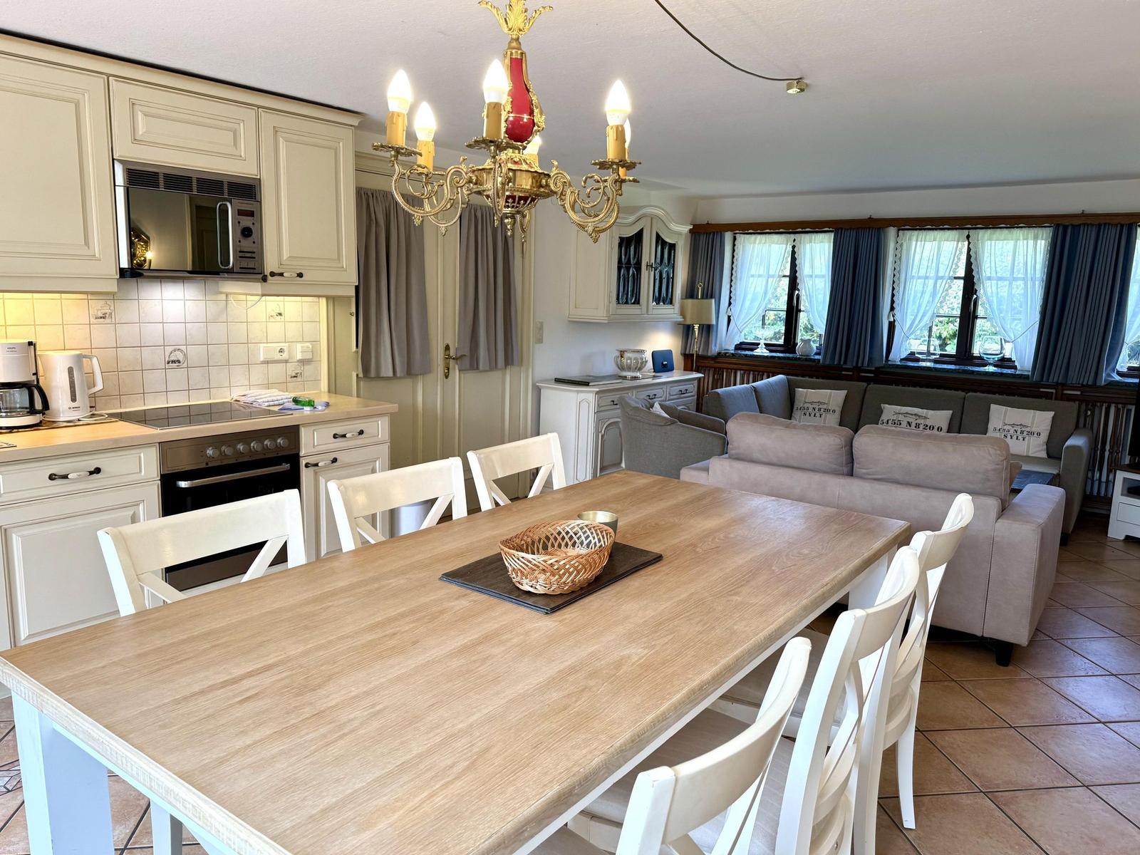 Dining area with table and chairs, kitchen, and living area with sofa and windows.