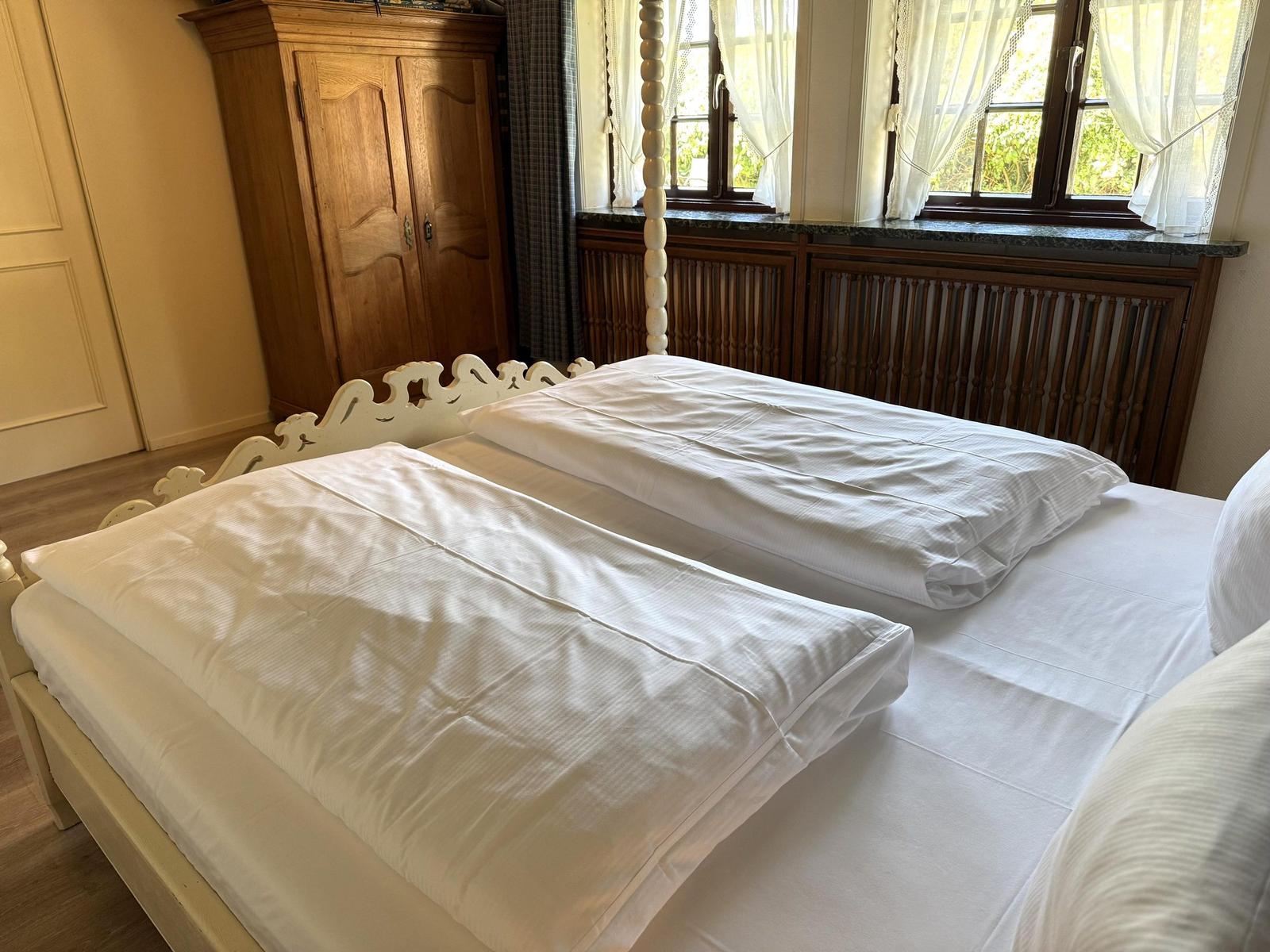 Bedroom with double bed, wooden wardrobe, and window with view of greenery.