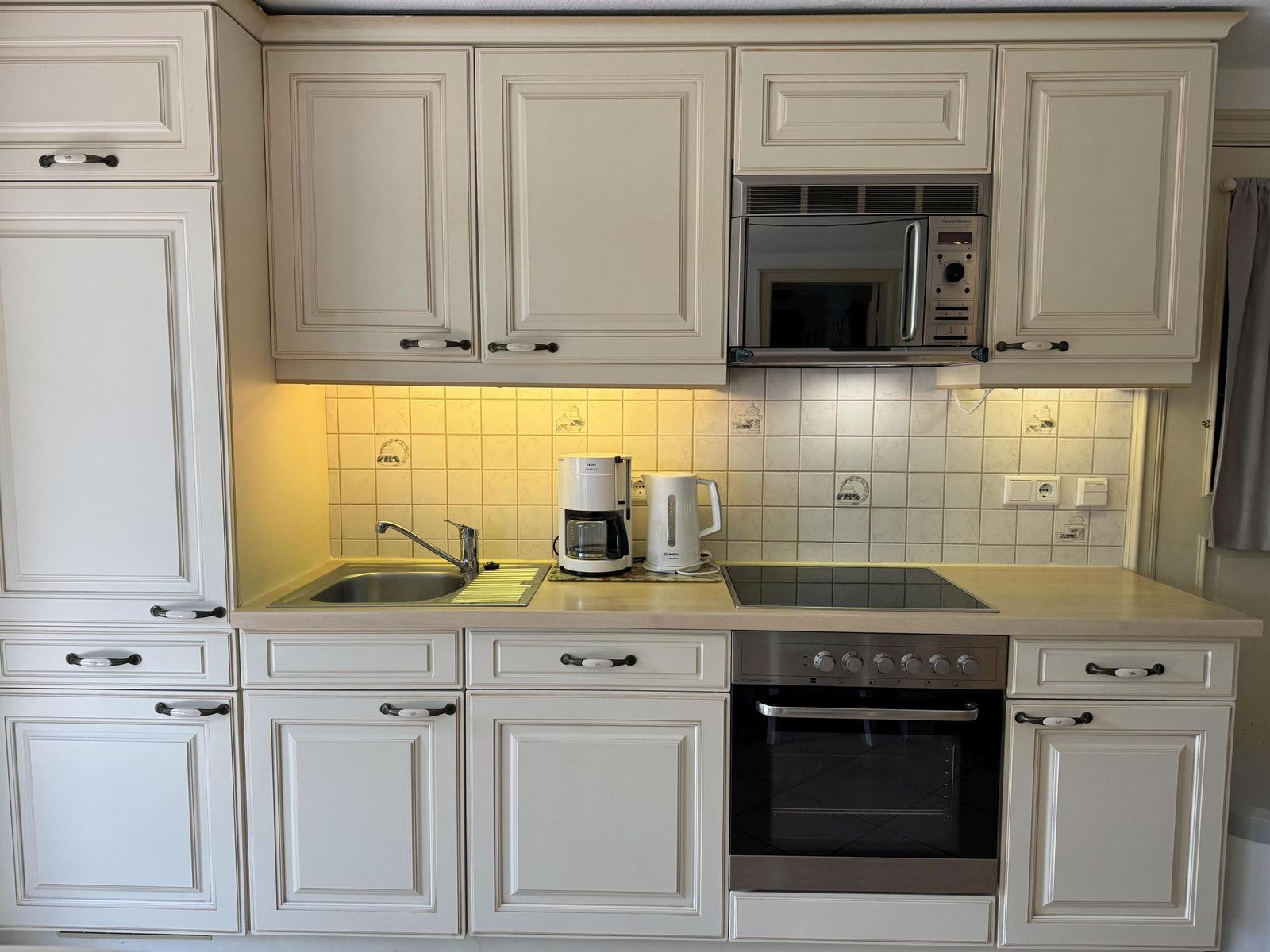 Kitchen with white cabinets, stove, microwave, and coffee maker.