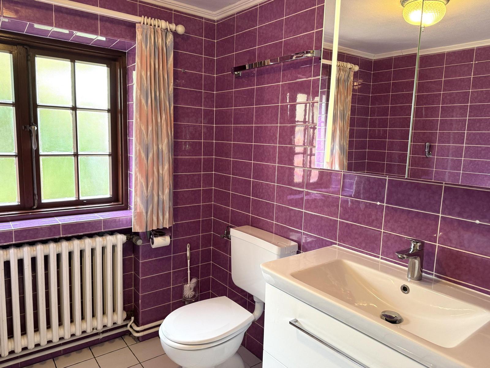Bathroom with purple tiles, sink, toilet, and window.