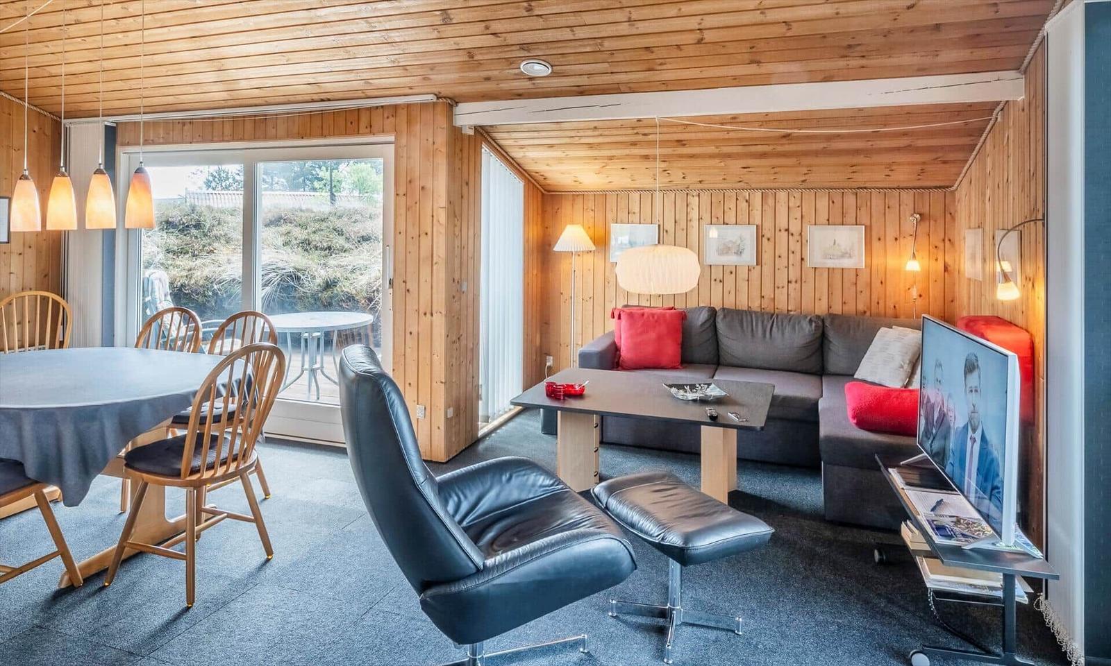 Wohn- und Essbereich mit Sofa, Esstisch und Fernseher. Holzwände und -decke.