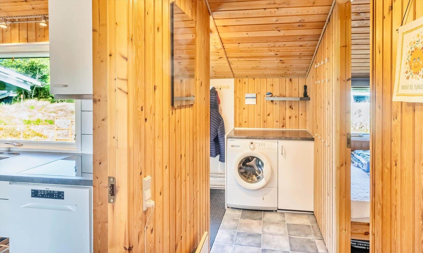 Waschmaschine in einem Holzraum mit Küchenbereich und Schlafzimmer sichtbar.
