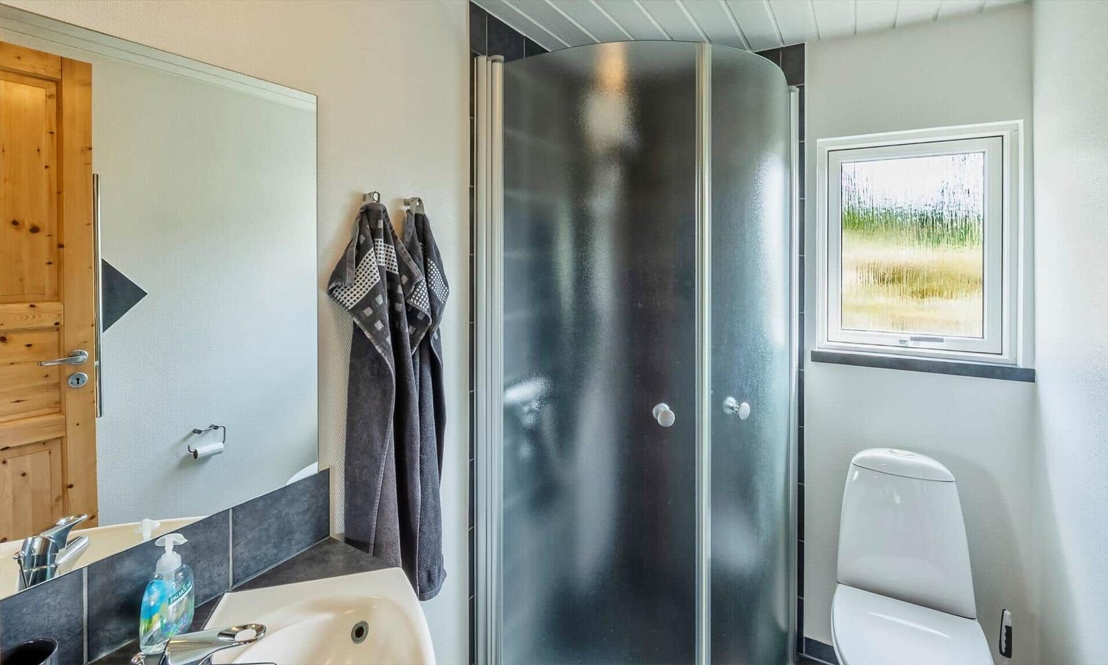 Badezimmer mit Dusche, Waschbecken und Toilette. Fenster mit grünem Blick.