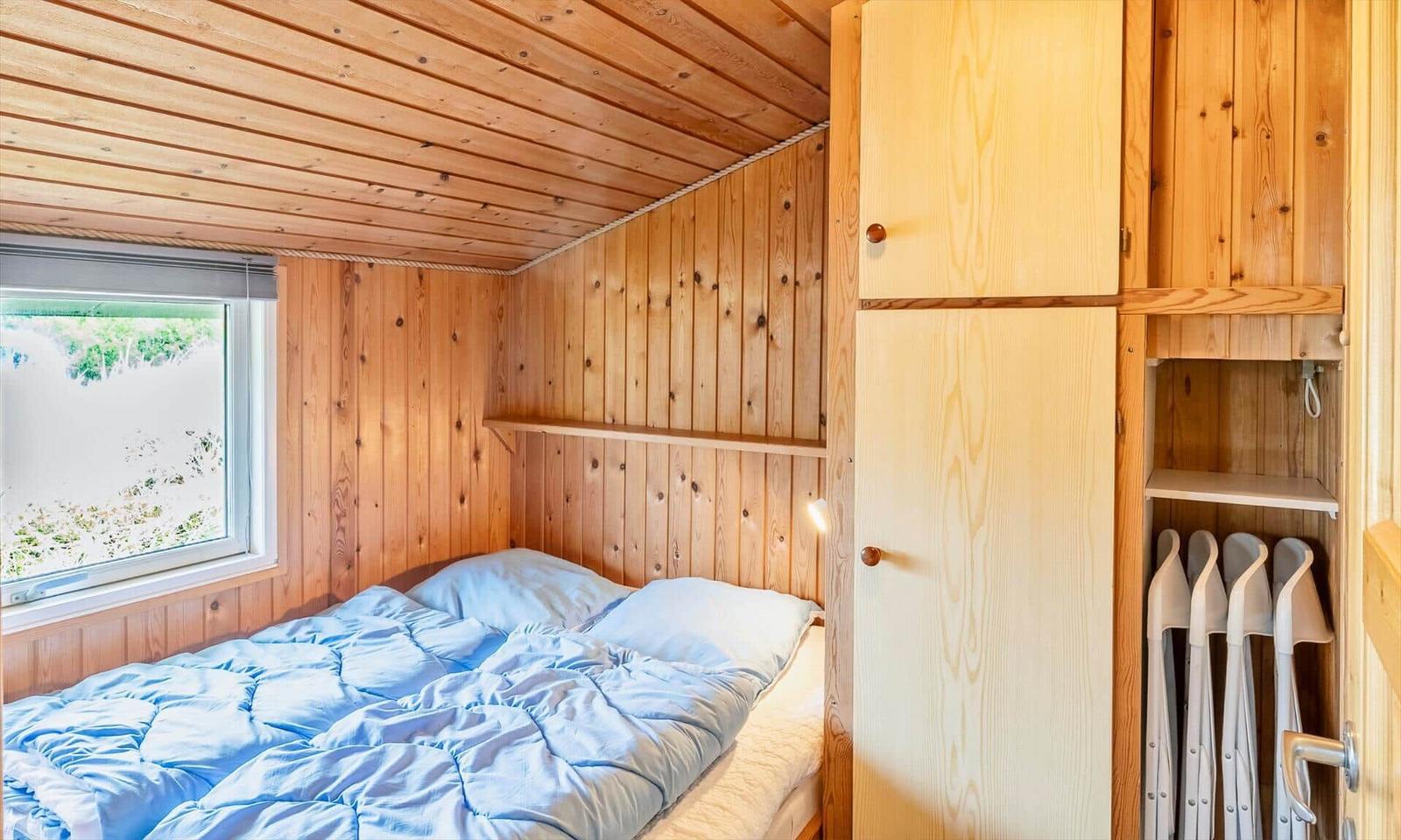 Schlafzimmer mit Holzwand, Bett und Kleiderschrank. Fenster zeigt Außenbereich.
