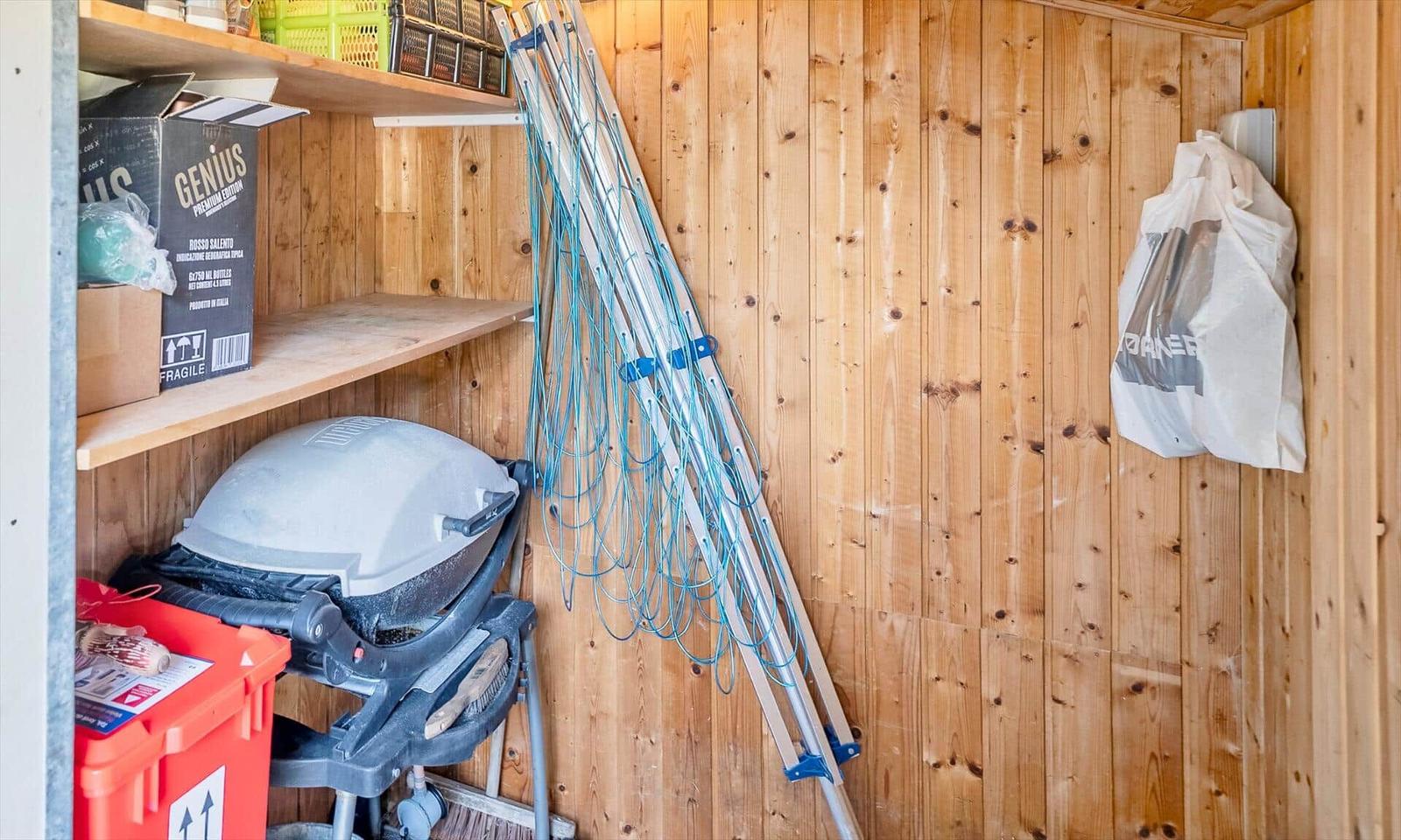 Holzvertäfelte Garage mit Regalen, Grill, Leiter und Einkaufstasche.