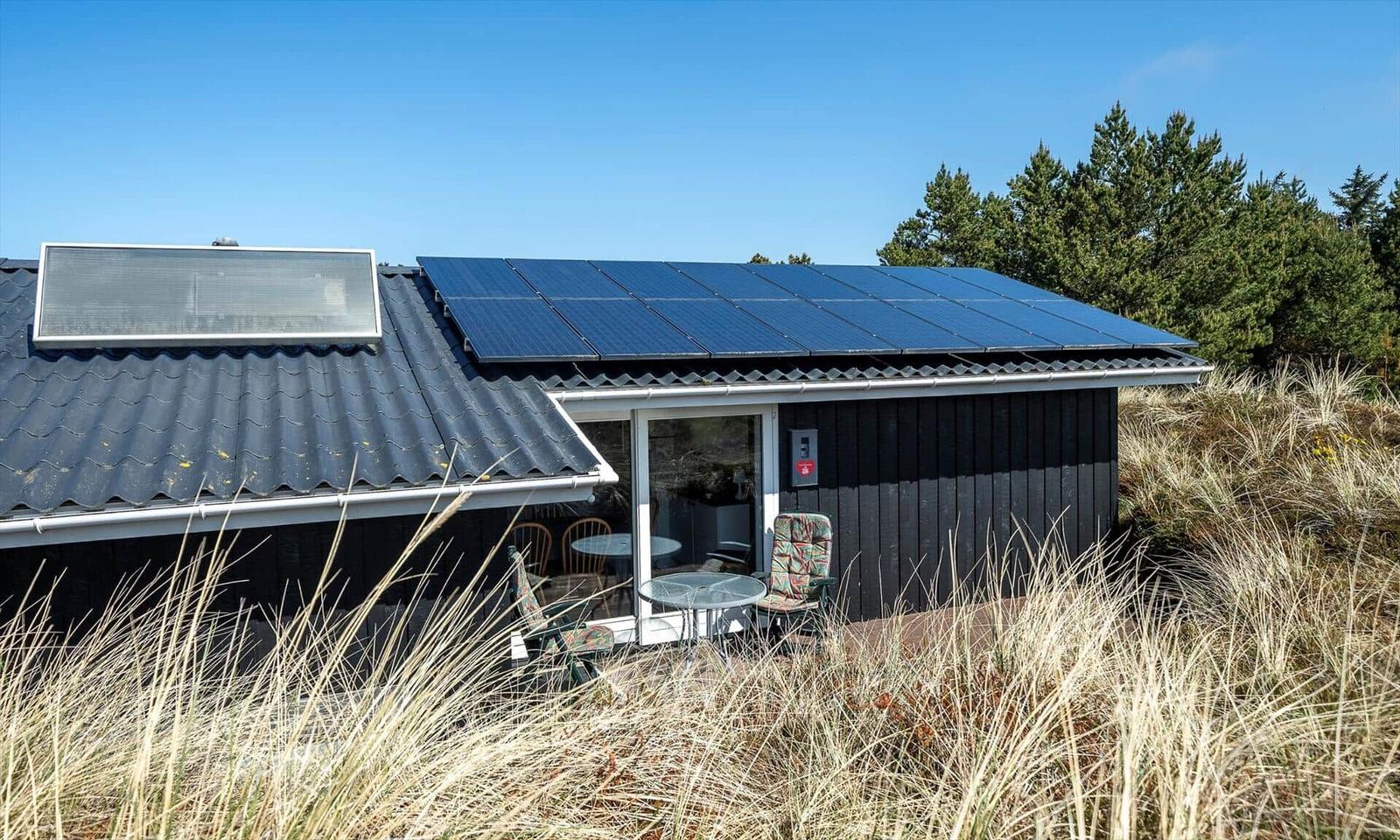 Ein Haus mit Solarpanel auf dem Dach und einer Terrasse mit Stühlen und Tisch.