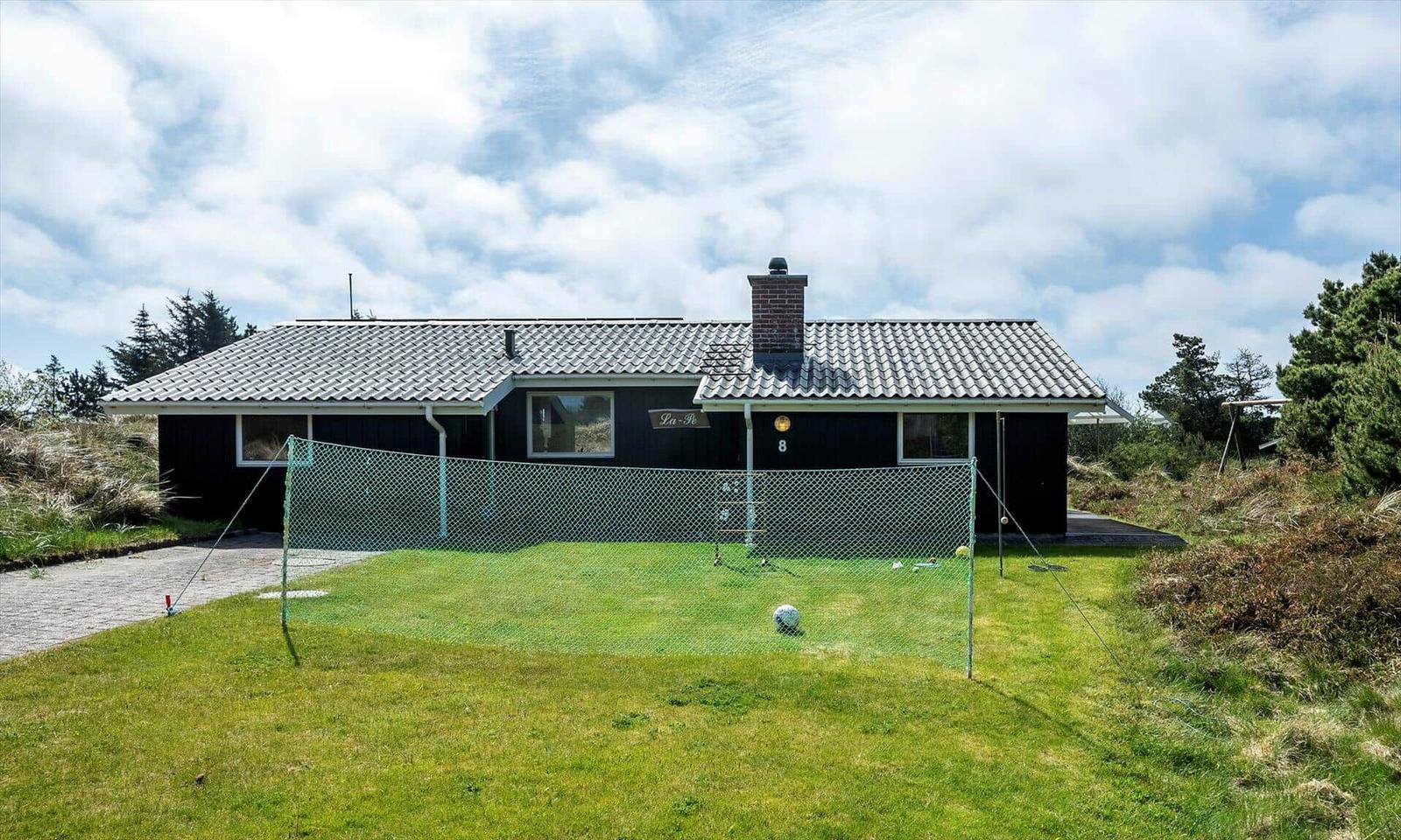 Schwarzes Haus mit Tennisnetz und grünem Rasen vorne.