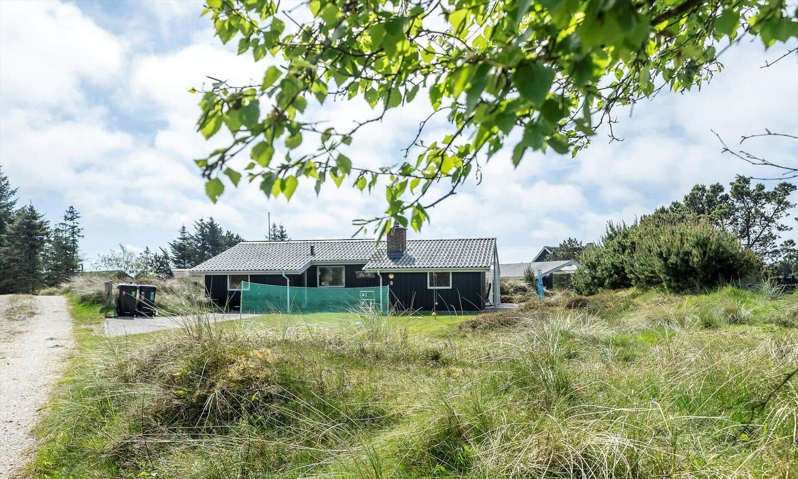 Ein dunkel gestrichenes Haus mit grünem Zaun und umliegender Graslandschaft.