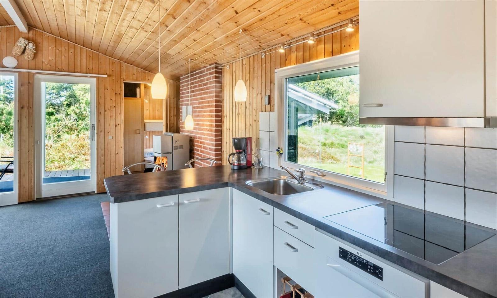 Küche mit Arbeitsfläche, Spüle und Fenster. Holzwände und Decke.