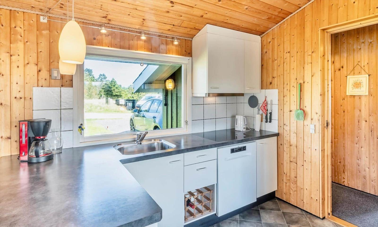 Küche mit Holzwand, Fenster, Spüle, Kaffeemaschine und Waschmaschine.