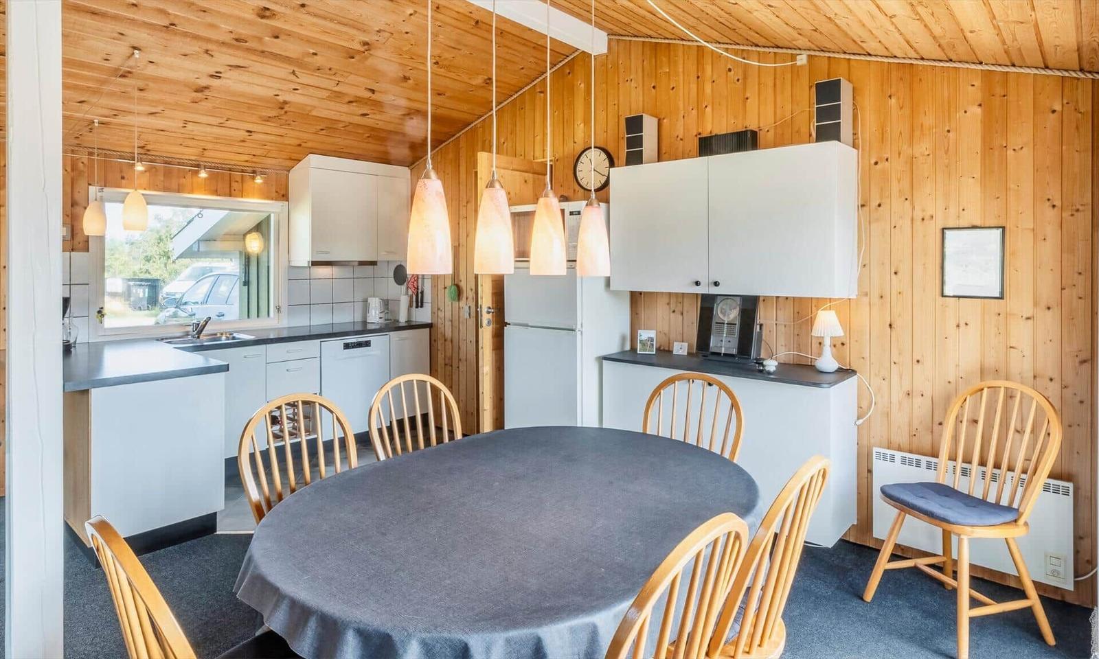 Küche und Essbereich mit runden Tisch und Holzstühlen, weißen Schränken und Holzwänden.